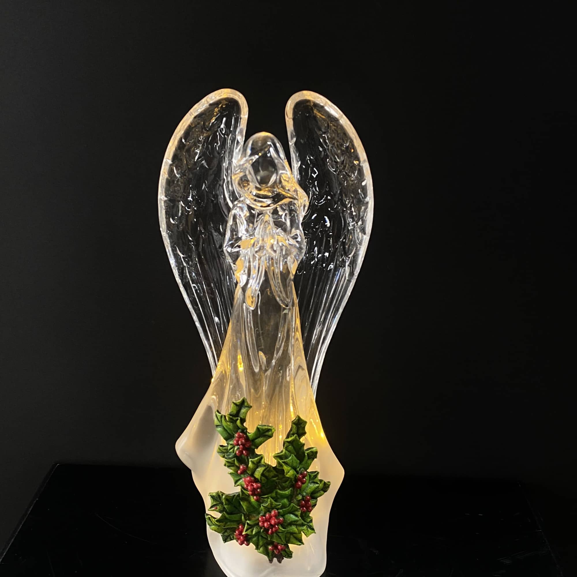 Glass angel figurine with holly decoration on a black background