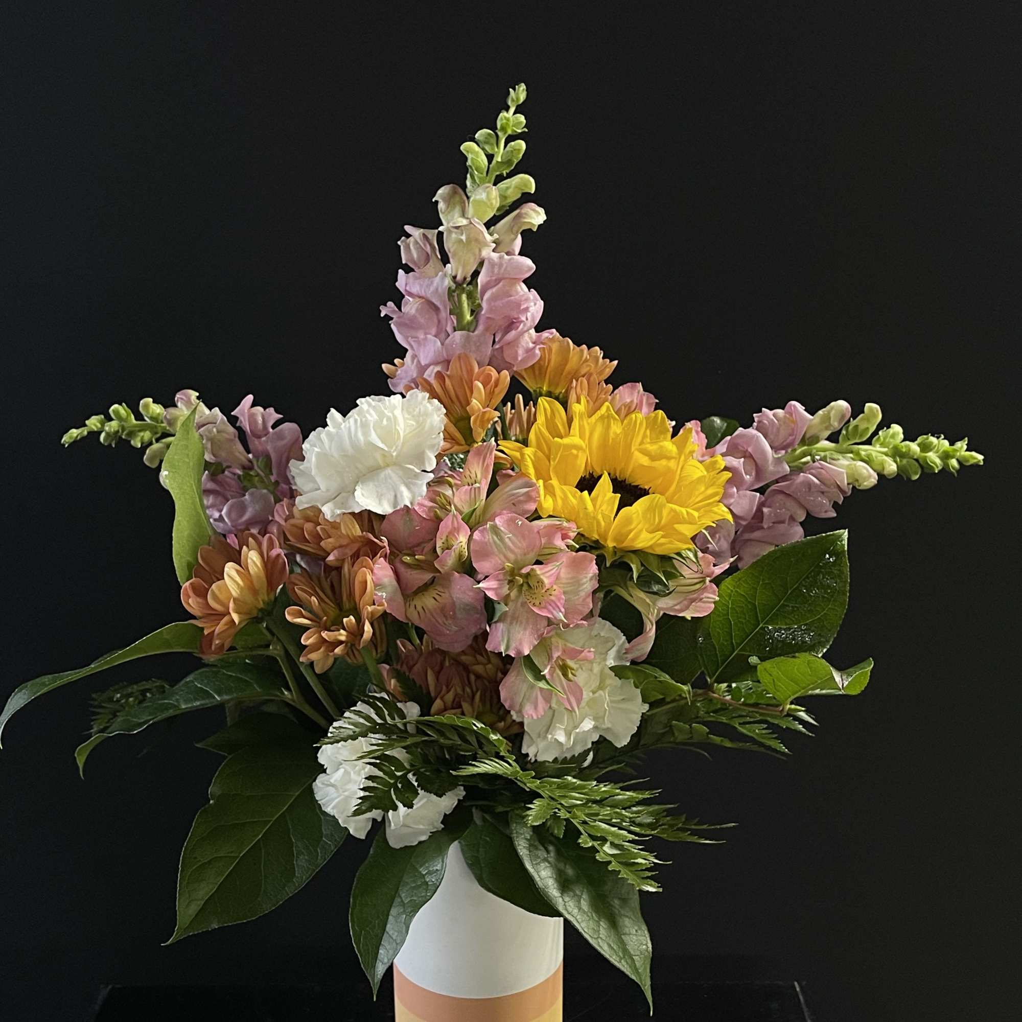 Mixed bouquet in a striped vase with sunflowers, snapdragons, and carnations