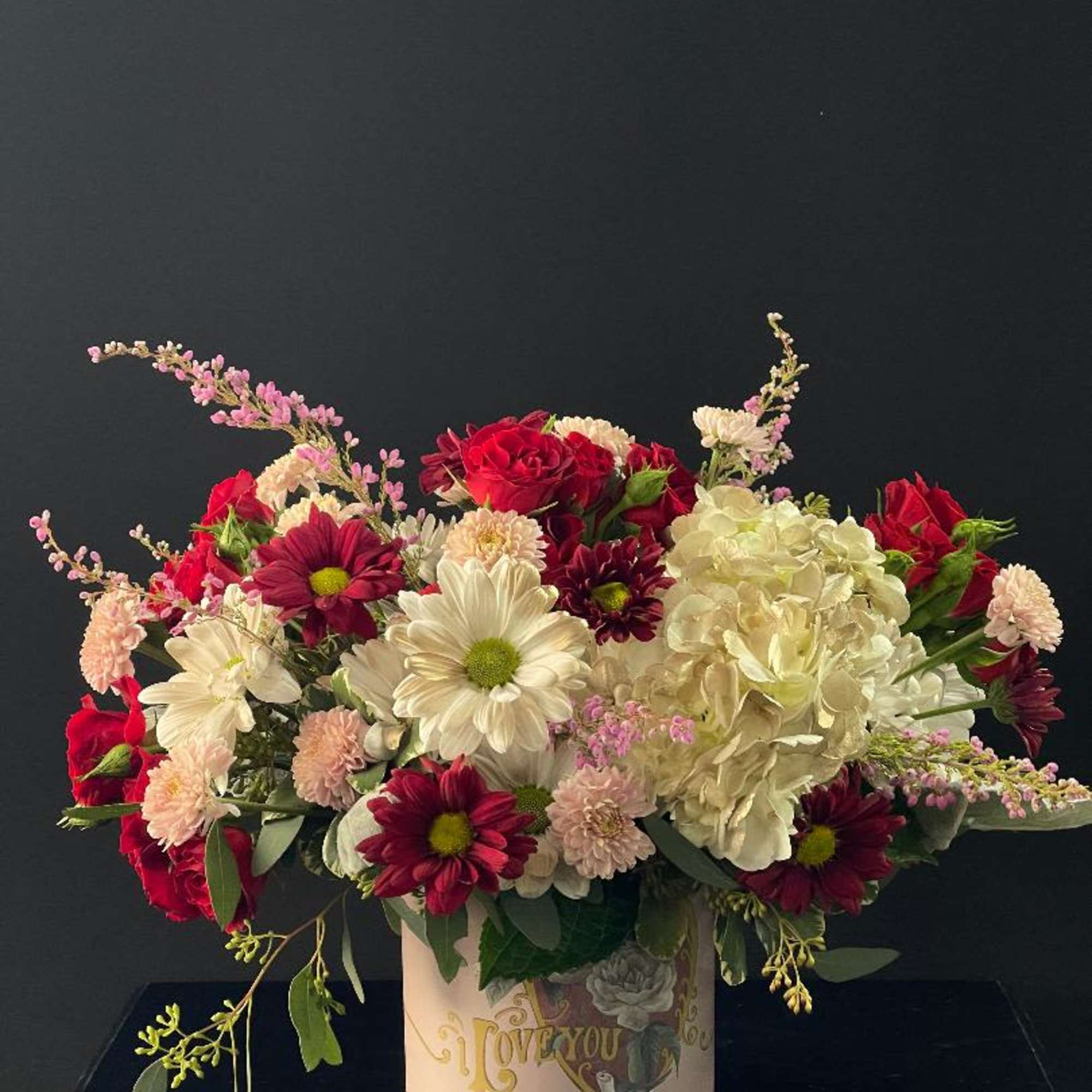 Mixed bouquet of red, white, and pink flowers in a decorative tin container