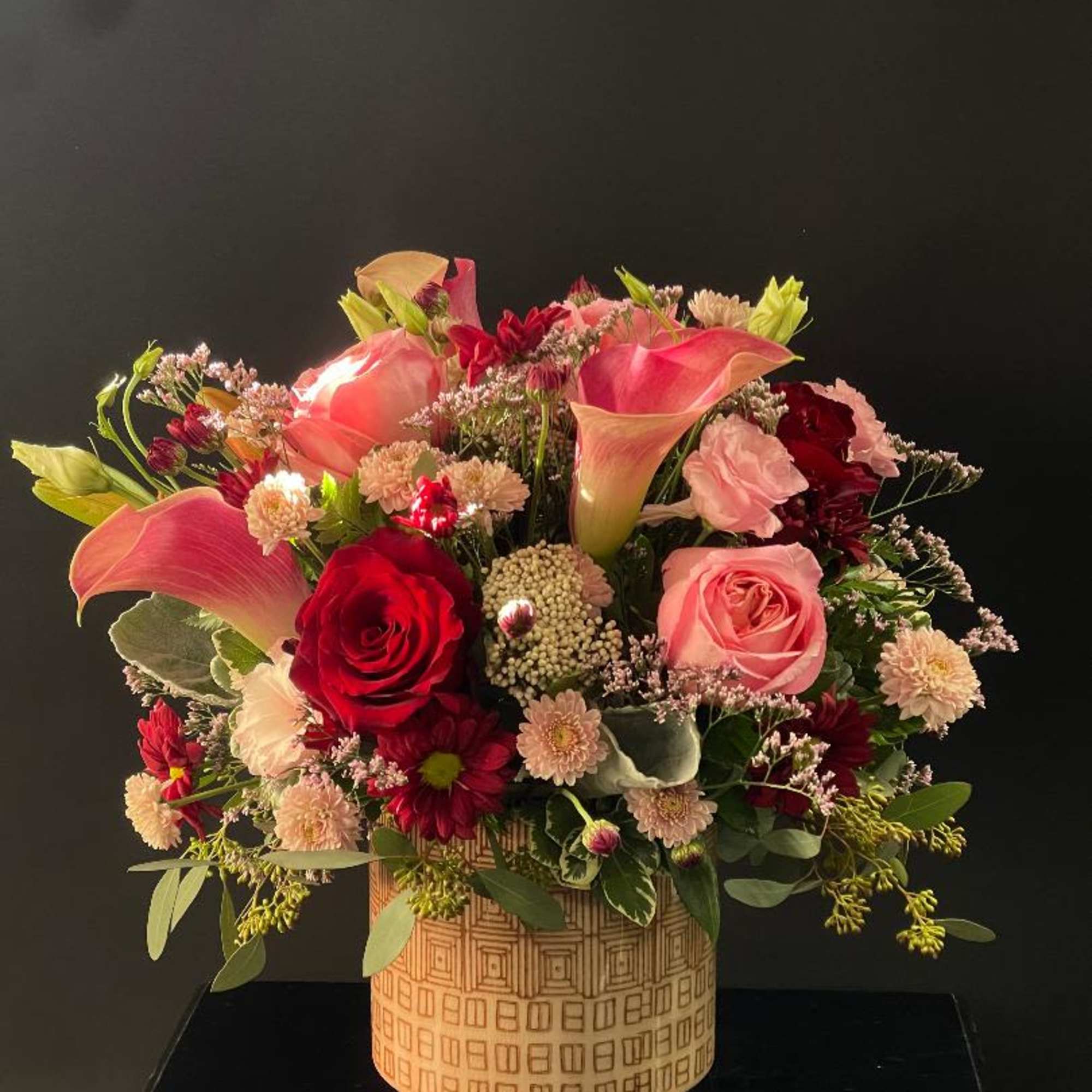 Pink calla lilies and roses arranged in a patterned vase