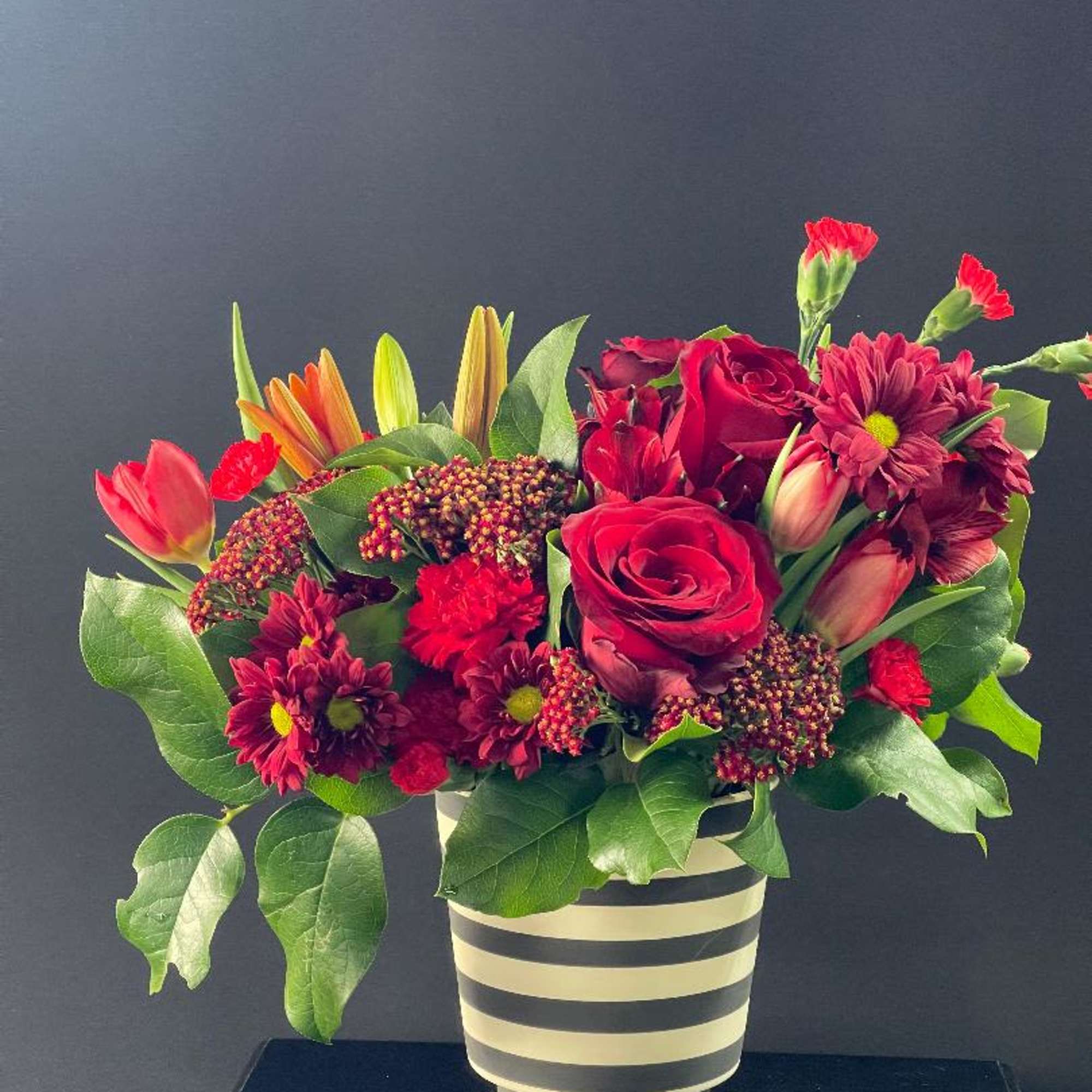 Red and burgundy mixed bouquet in a striped vase