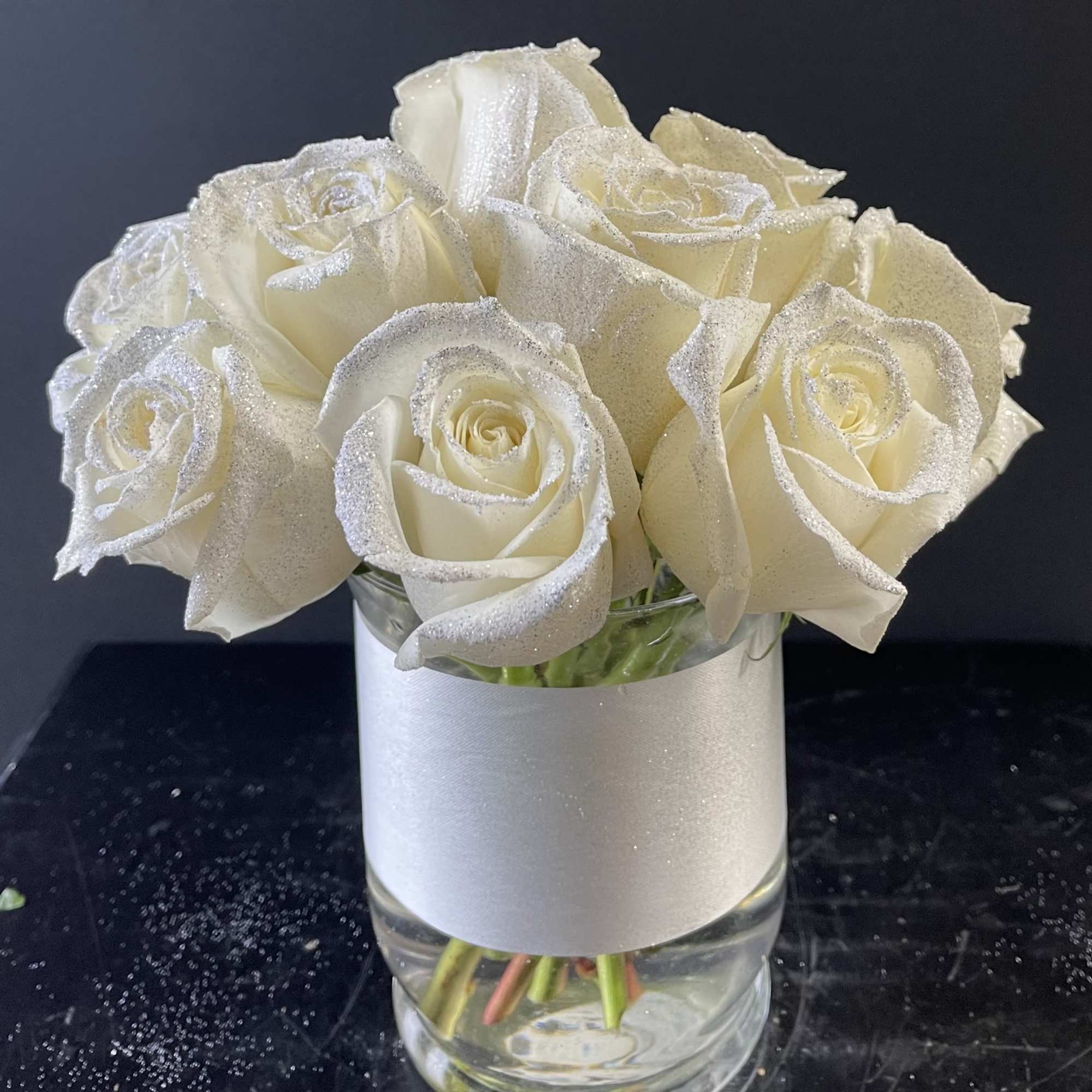 White roses in a clear glass vase with a silver wrap
