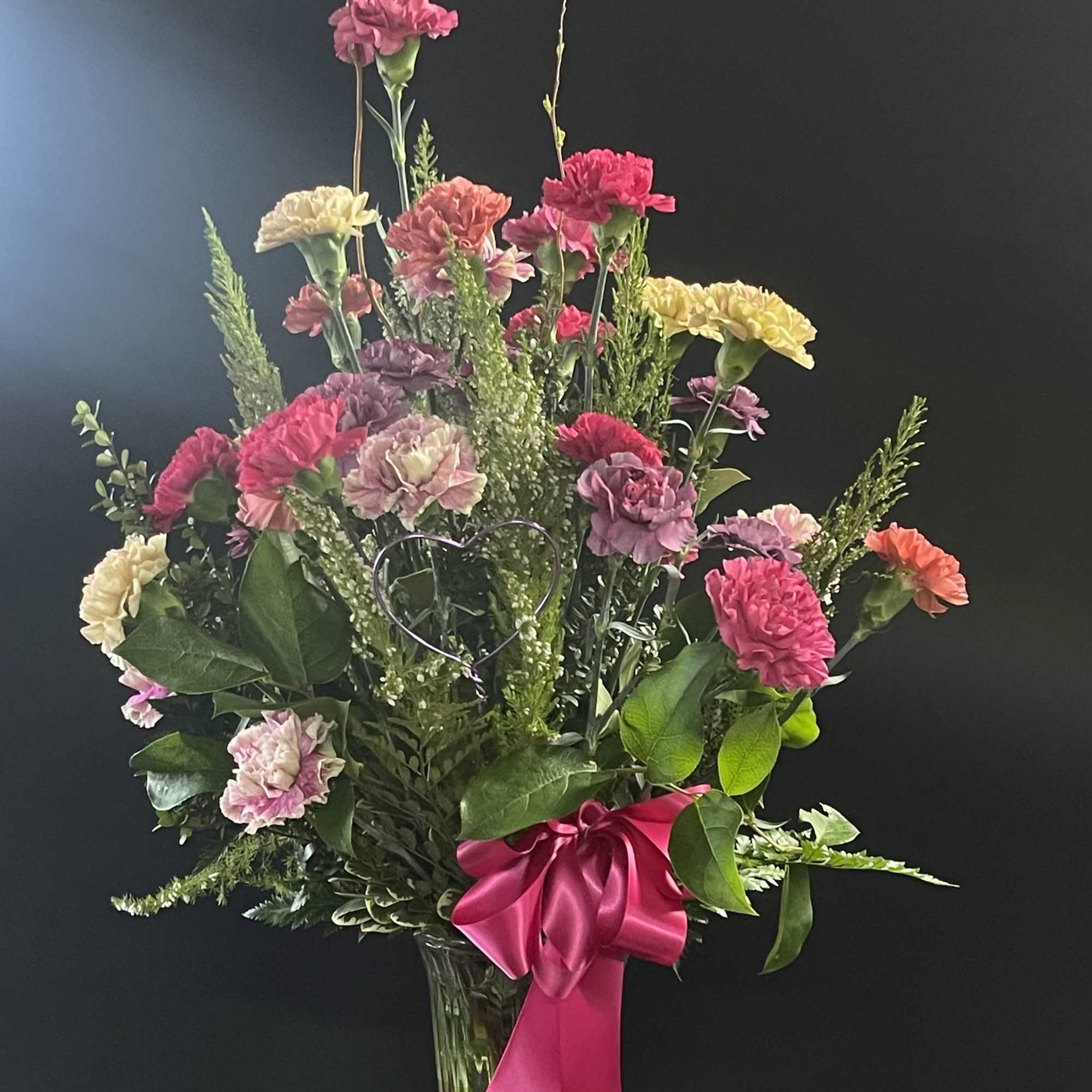 Tall mixed carnation arrangement in a clear vase with a pink ribbon