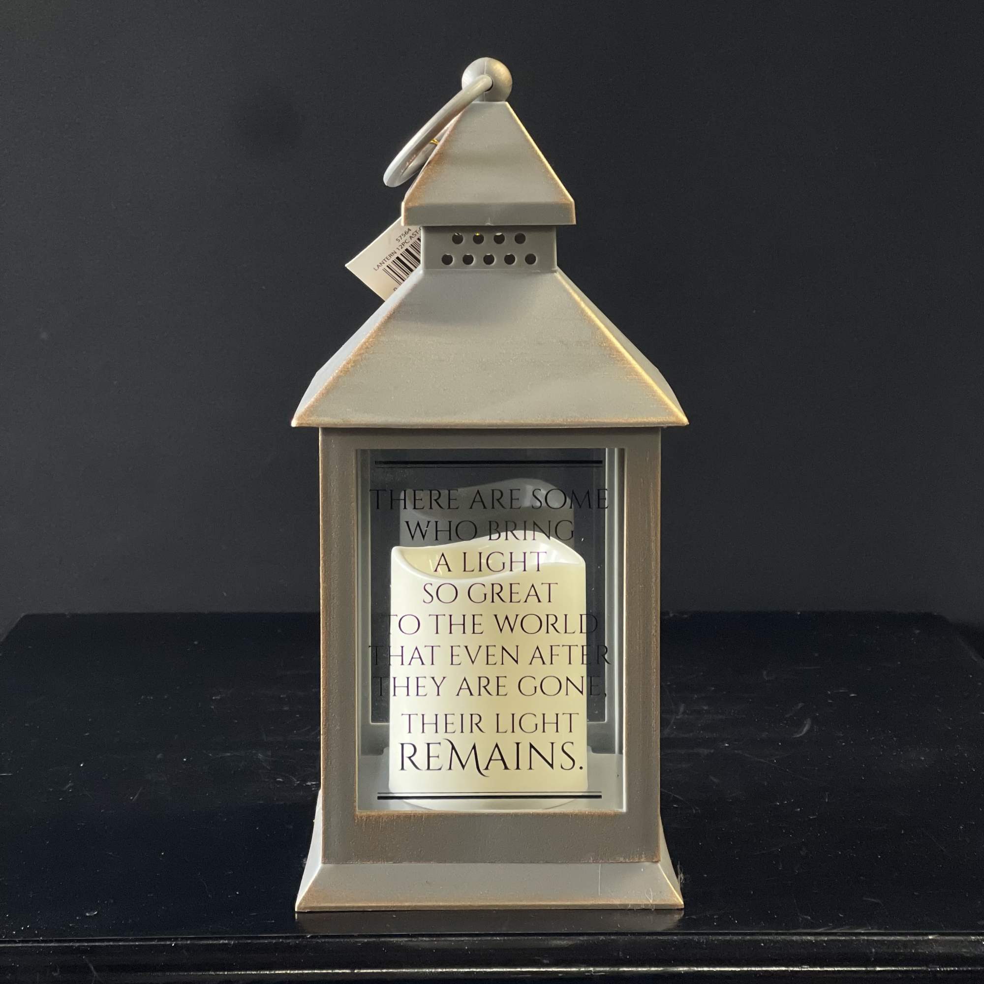 Beige metal lantern with glass sides, a memorial quote, and a white pillar candle inside.