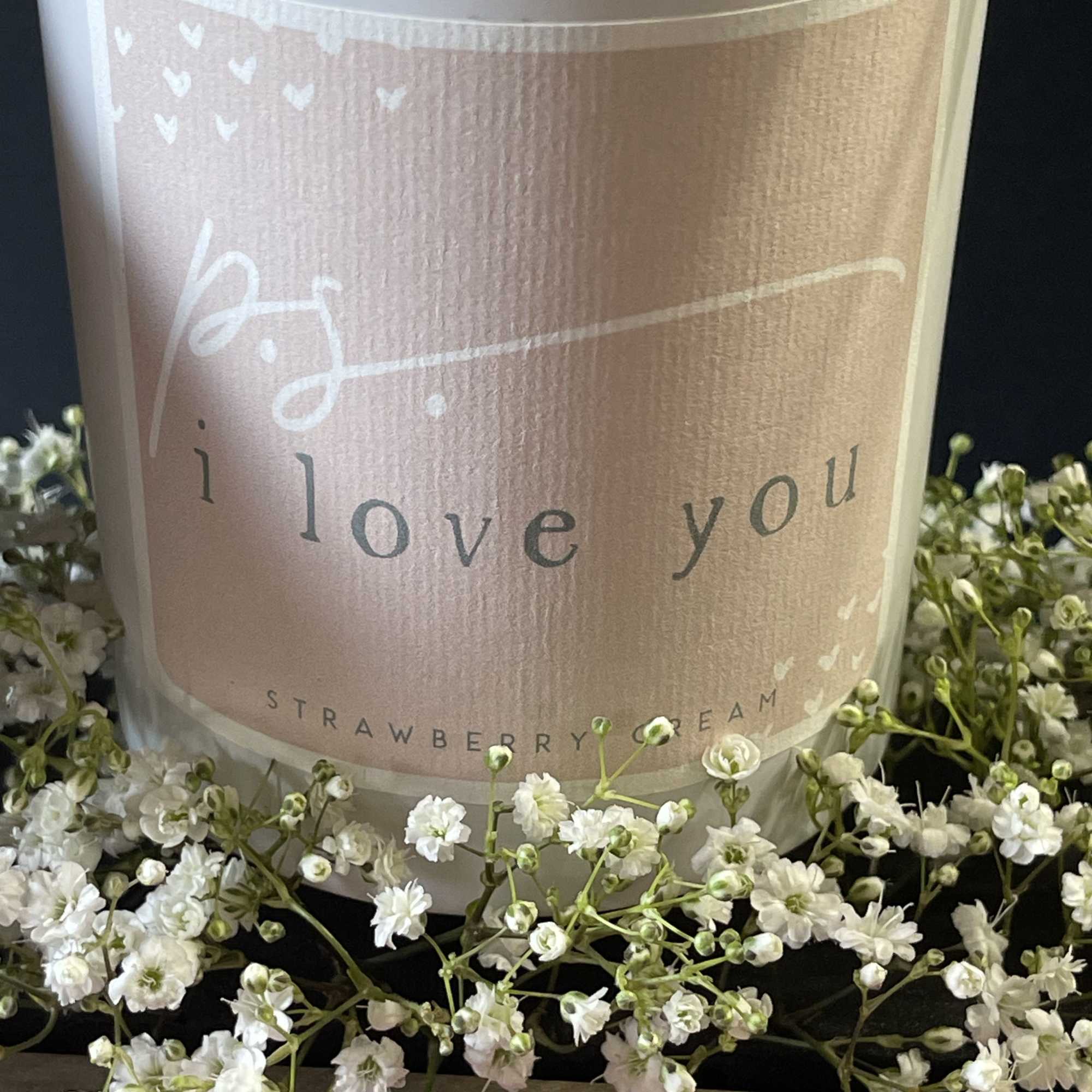 A candle jar labeled "i love you" surrounded by small white flowers