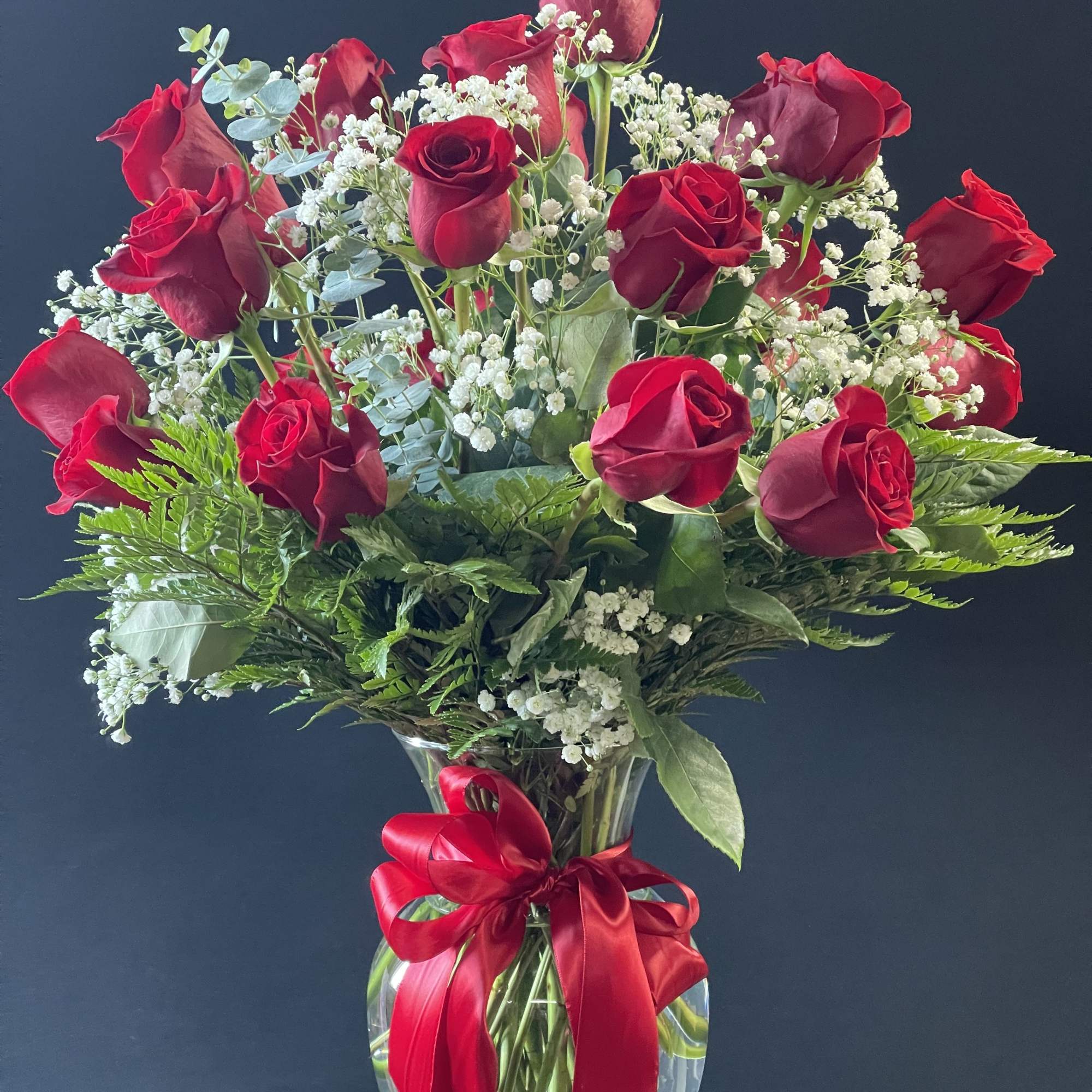 Red roses in a clear glass vase with a red ribbon