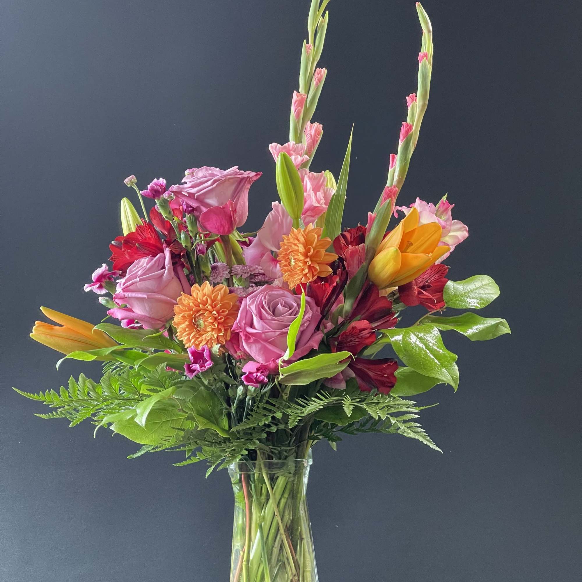 Mixed bouquet of pink, orange, and red flowers in a clear glass vase