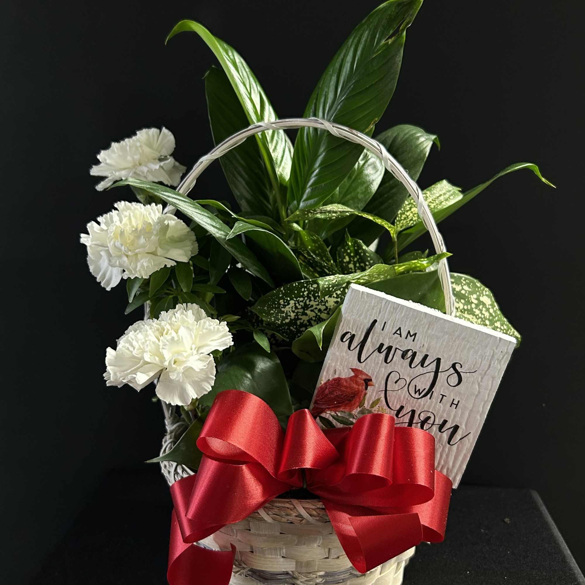 White carnations in a wicker basket with a red ribbon and card