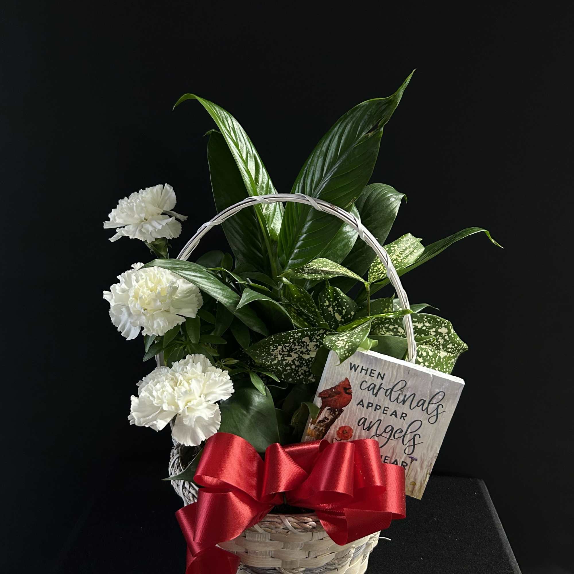 White carnations in a wicker basket with a red bow and sympathy sign