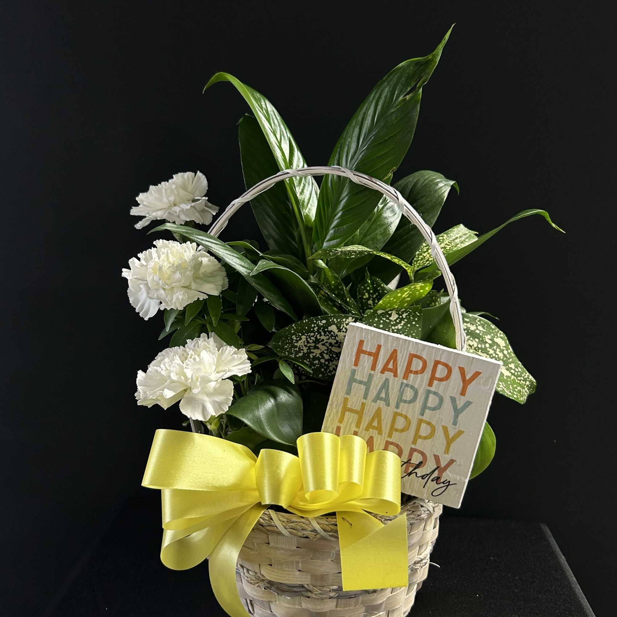 Basket arrangement with white carnations, green foliage, and a yellow ribbon
