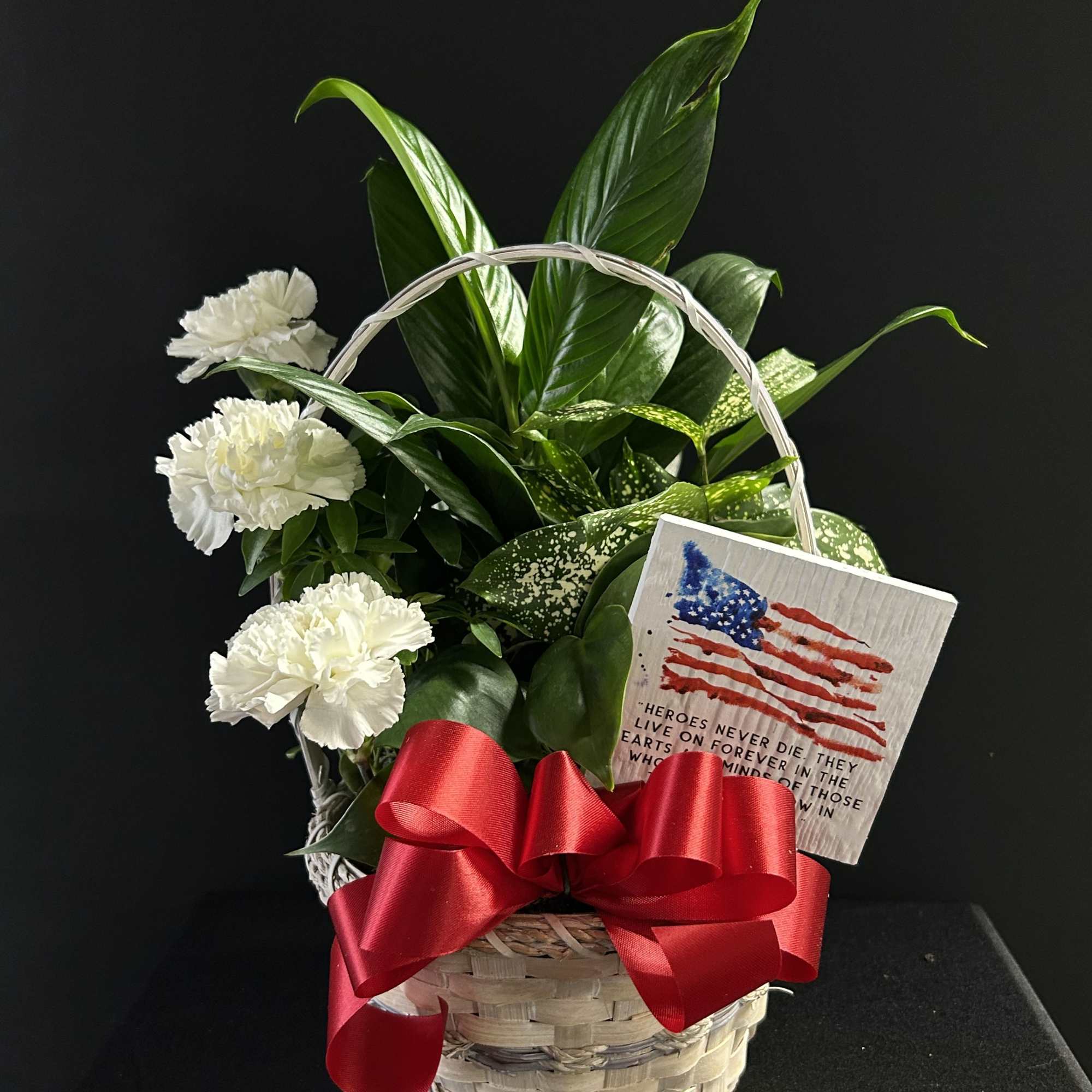 White carnations in a basket with a red ribbon and memorial card