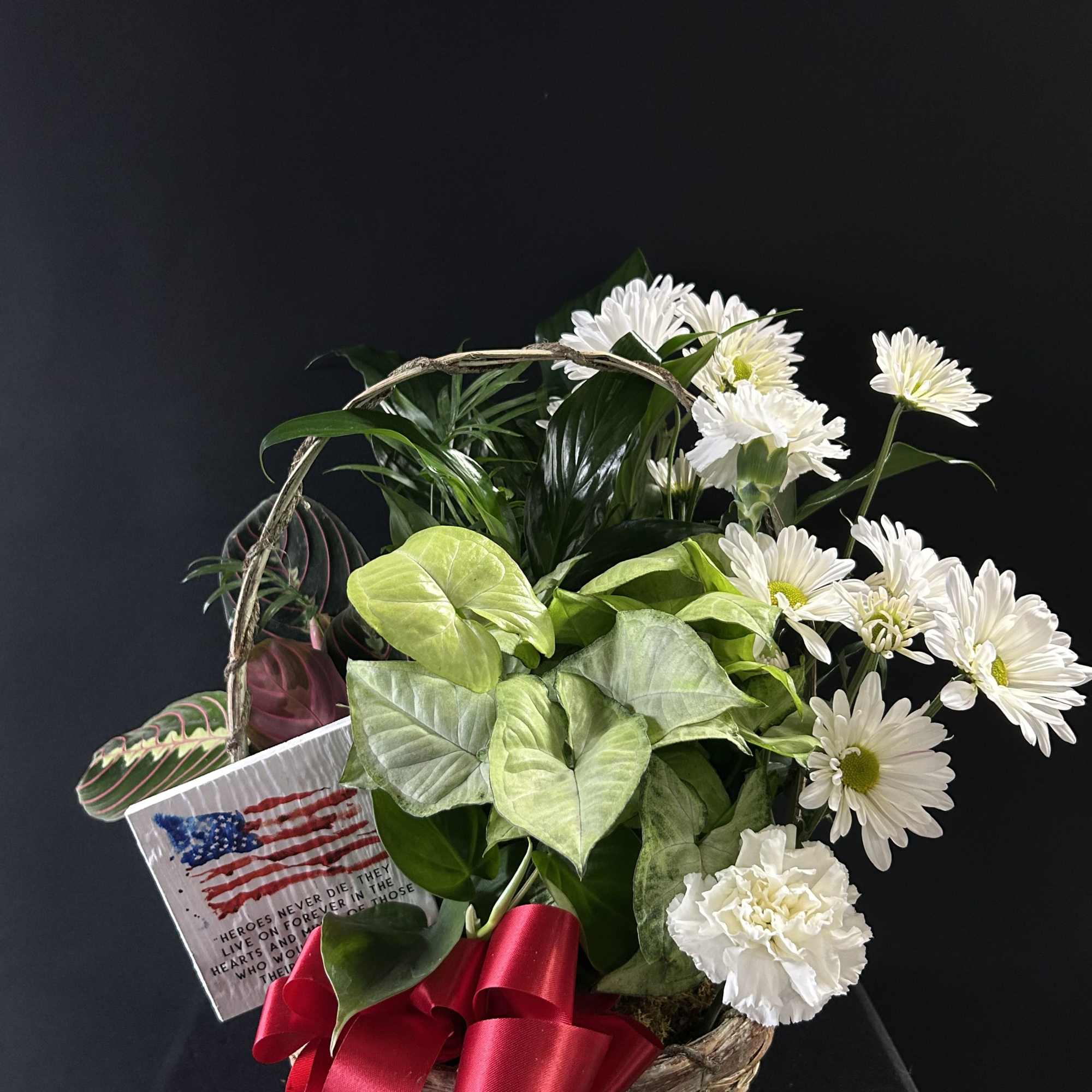 Basket arrangement with white daisies and green foliage, accented by a red ribbon