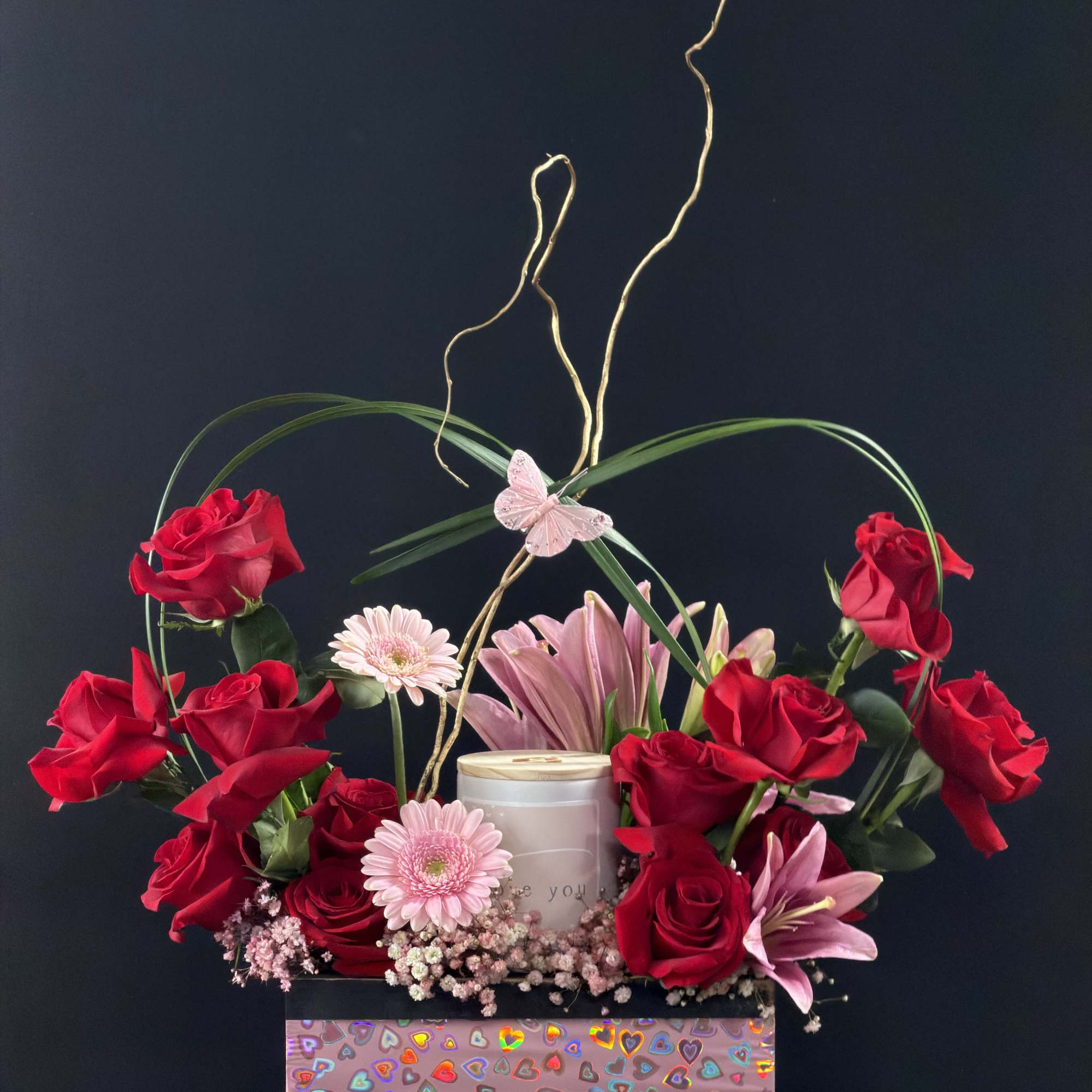 Red roses and pink lilies arranged in a decorative gift box with a butterfly accent.