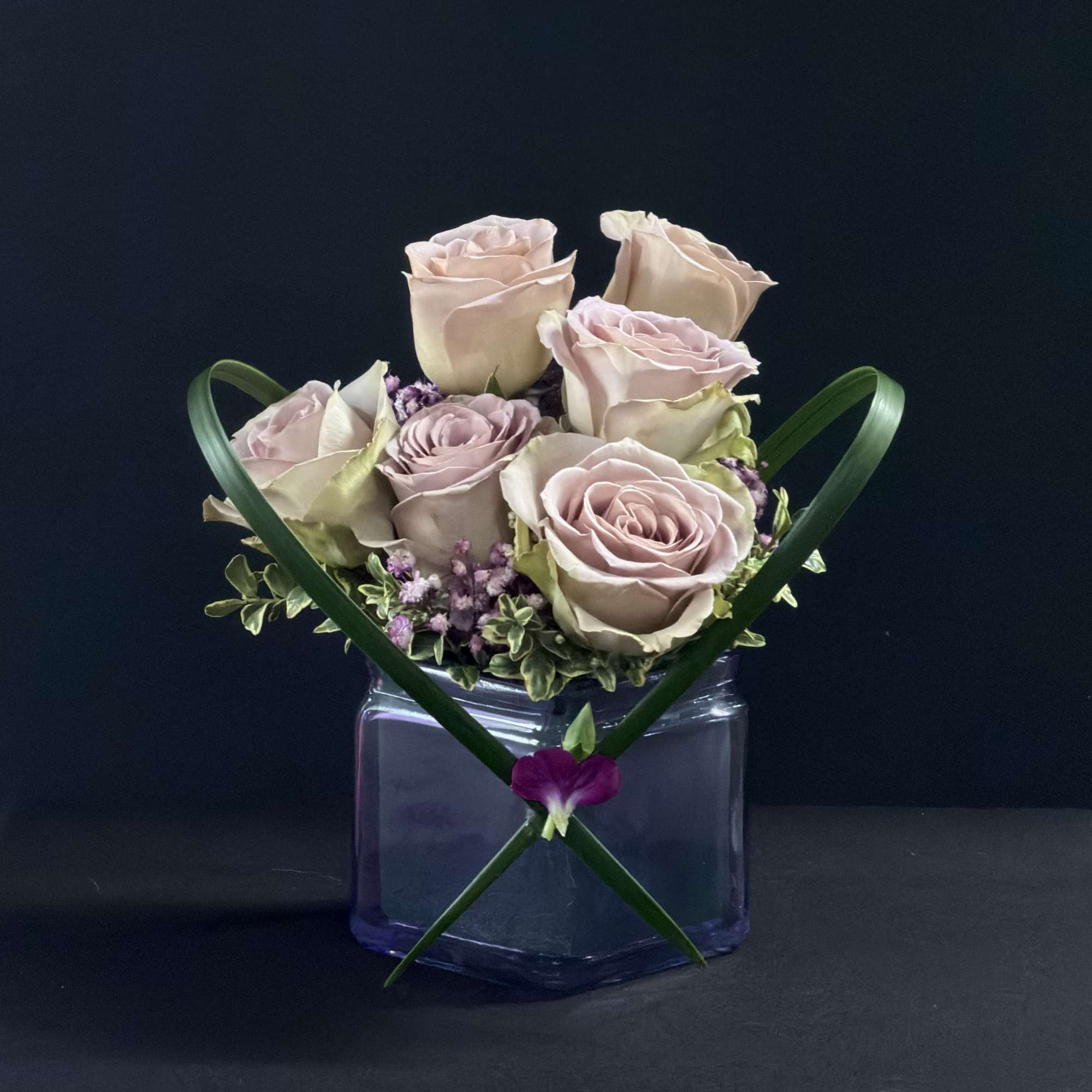 Blush roses arranged in a square glass vase with green ribbon accents