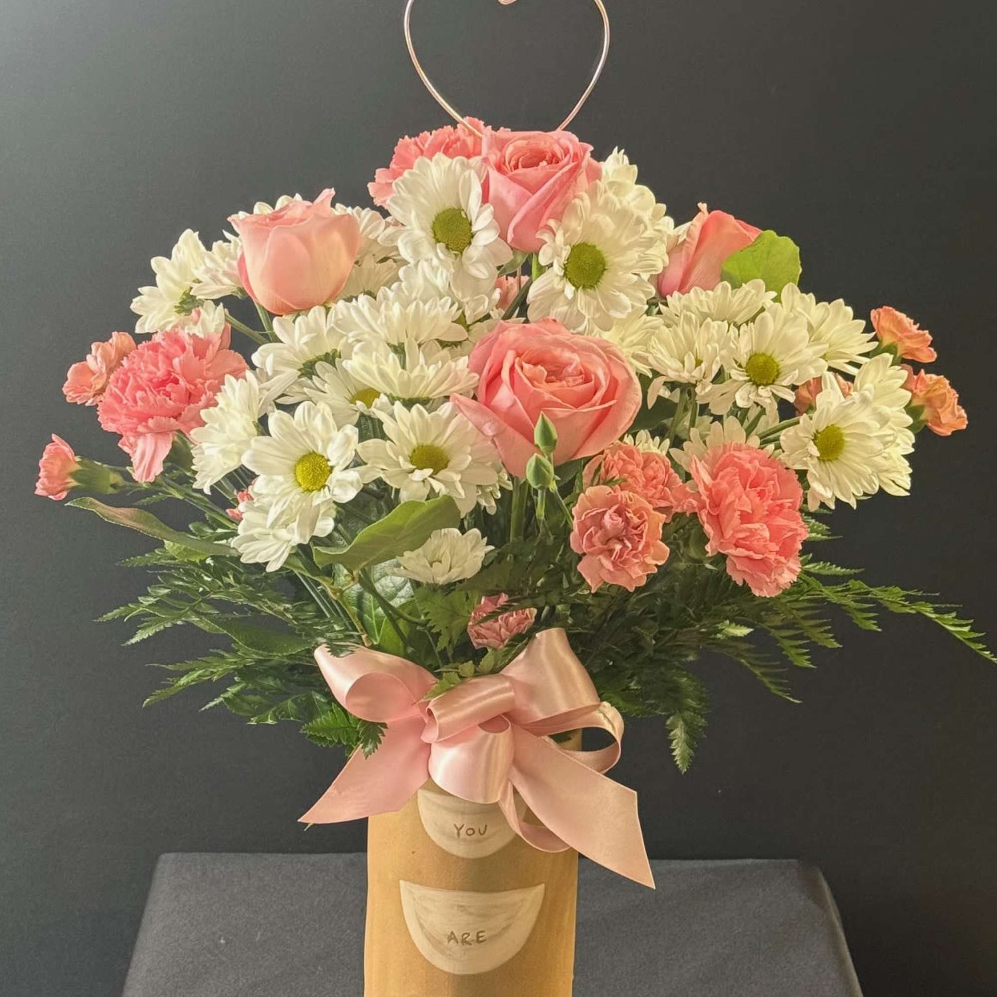 Pink roses and white daisies in a gold vase with a heart topper