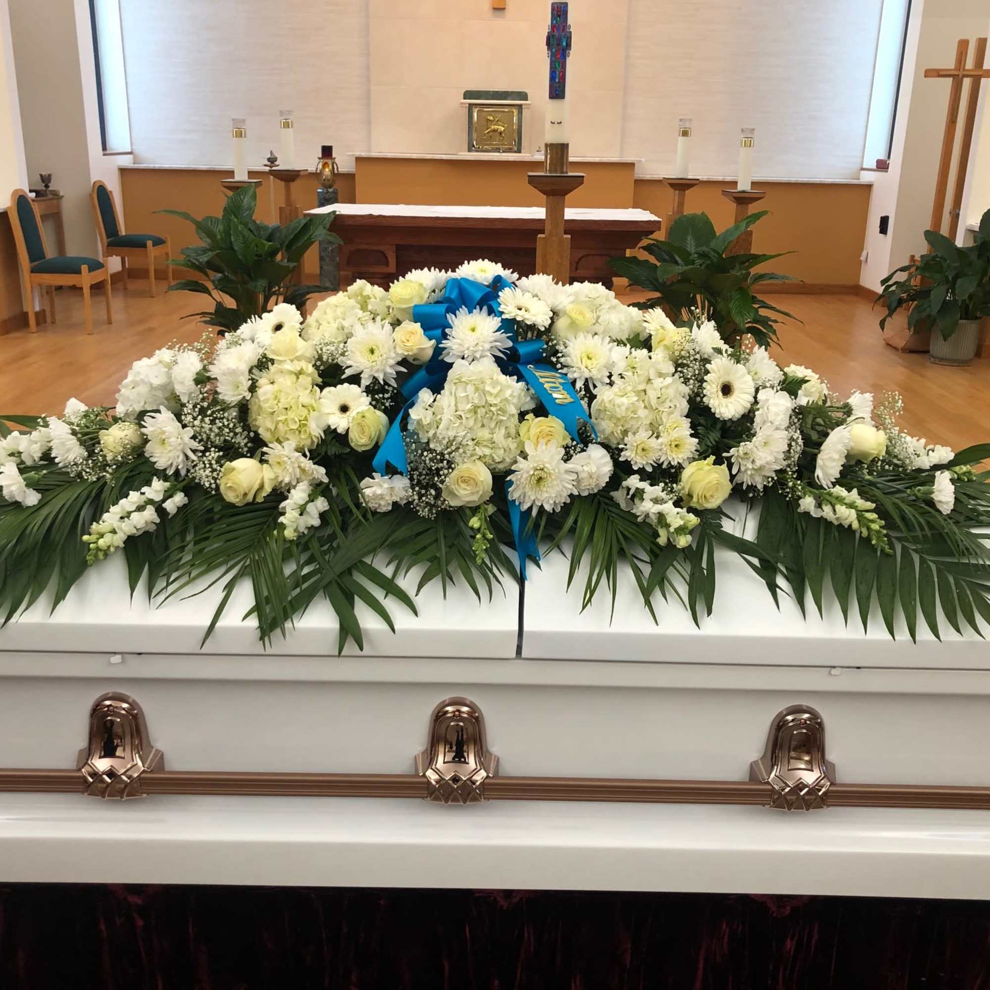 White floral casket spray with blue ribbon on a white casket