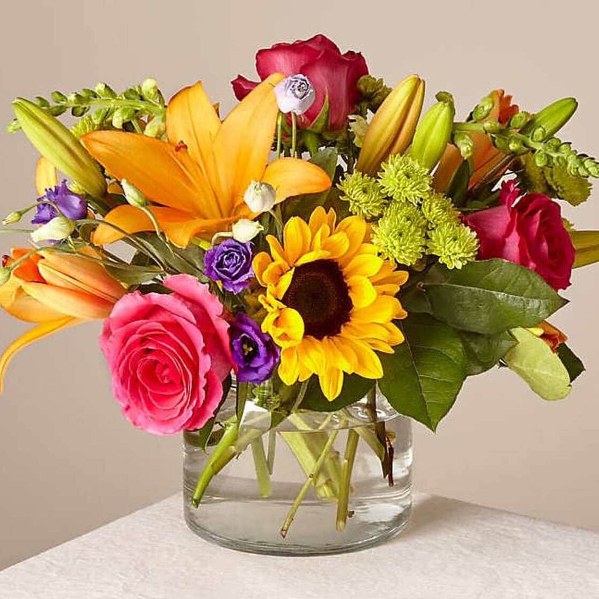 Mixed bouquet of roses, lilies, and a sunflower in a glass vase