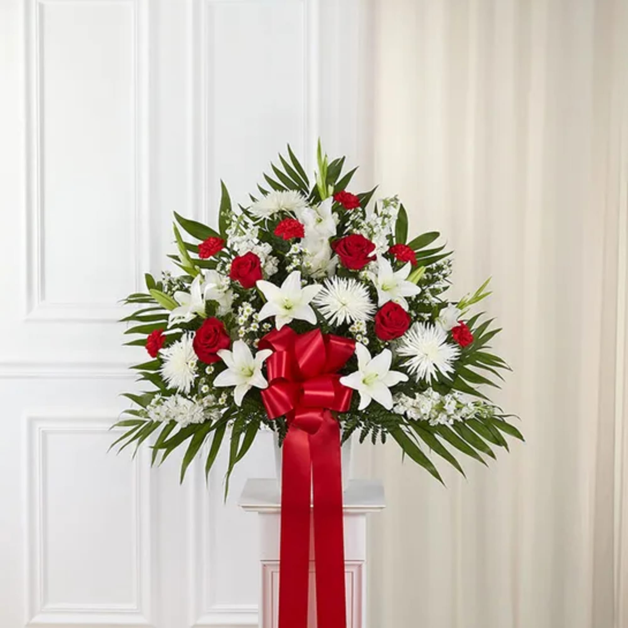 Standing floral spray with red roses, white lilies, and a red ribbon