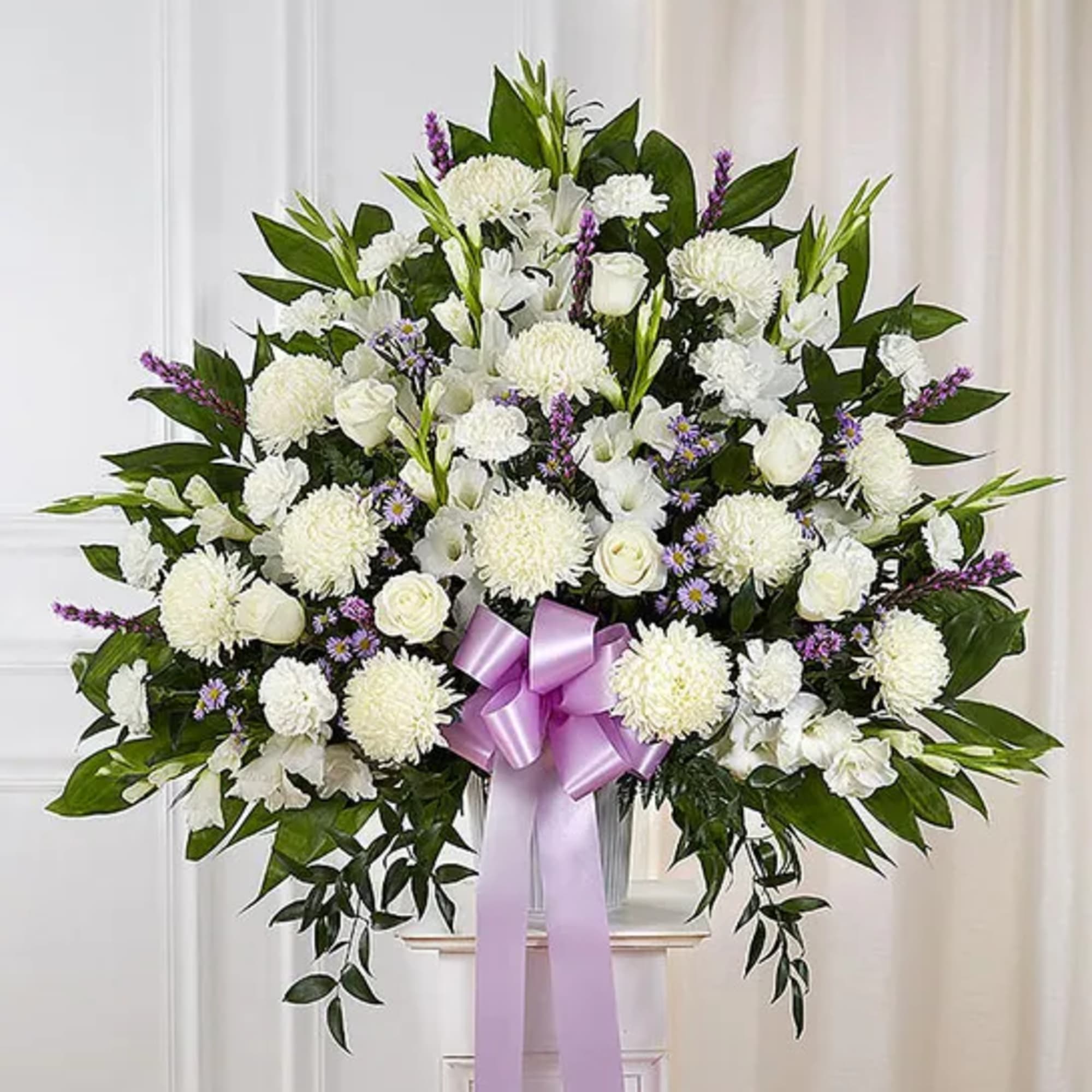White funeral spray with purple ribbon and mixed blooms on a stand