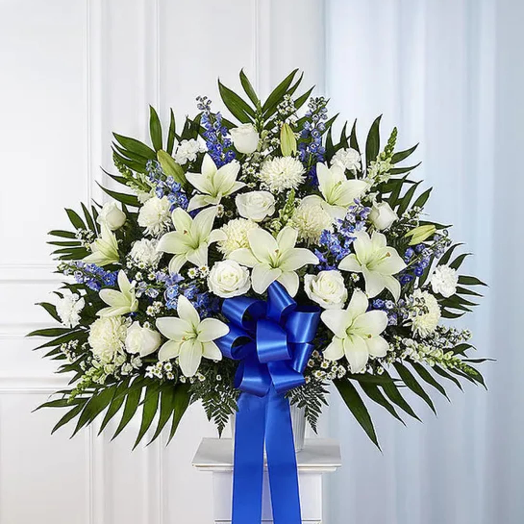 White lilies and roses in a large standing spray with a blue ribbon