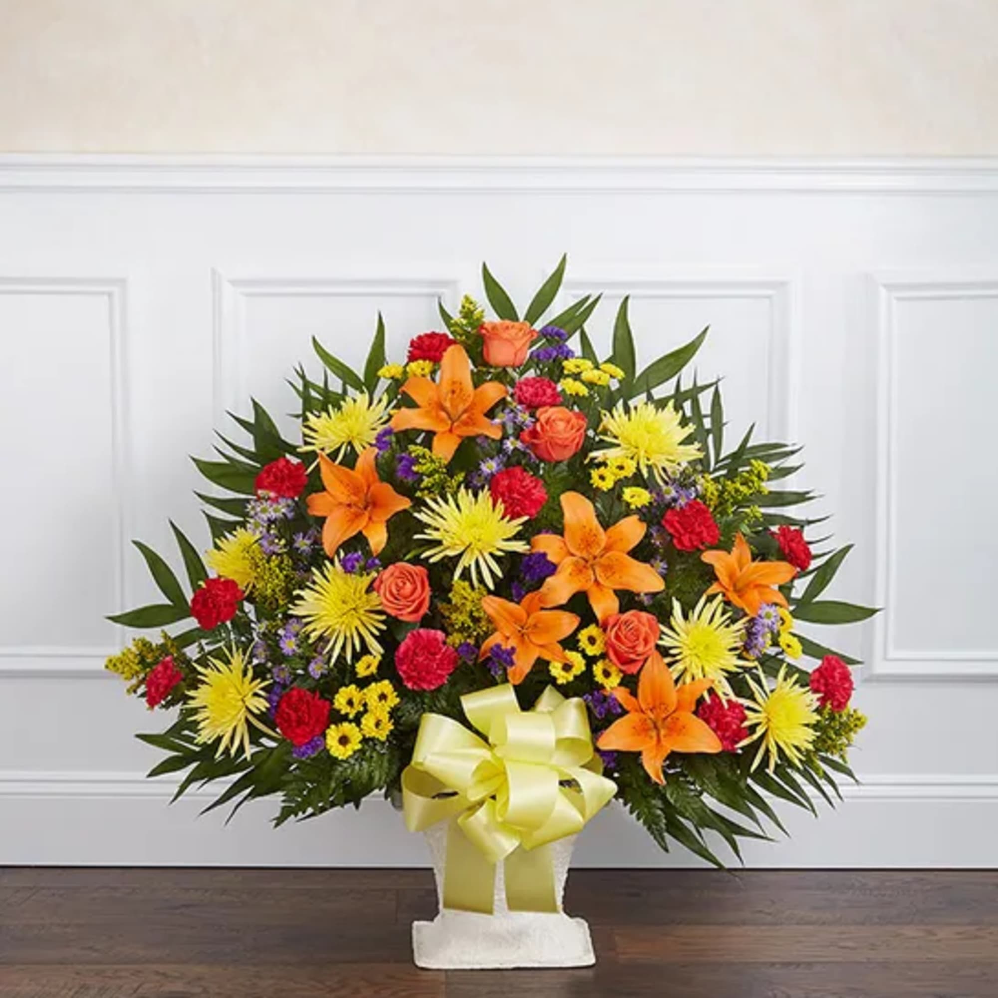 Bright mixed flower arrangement in a white vase with a yellow ribbon