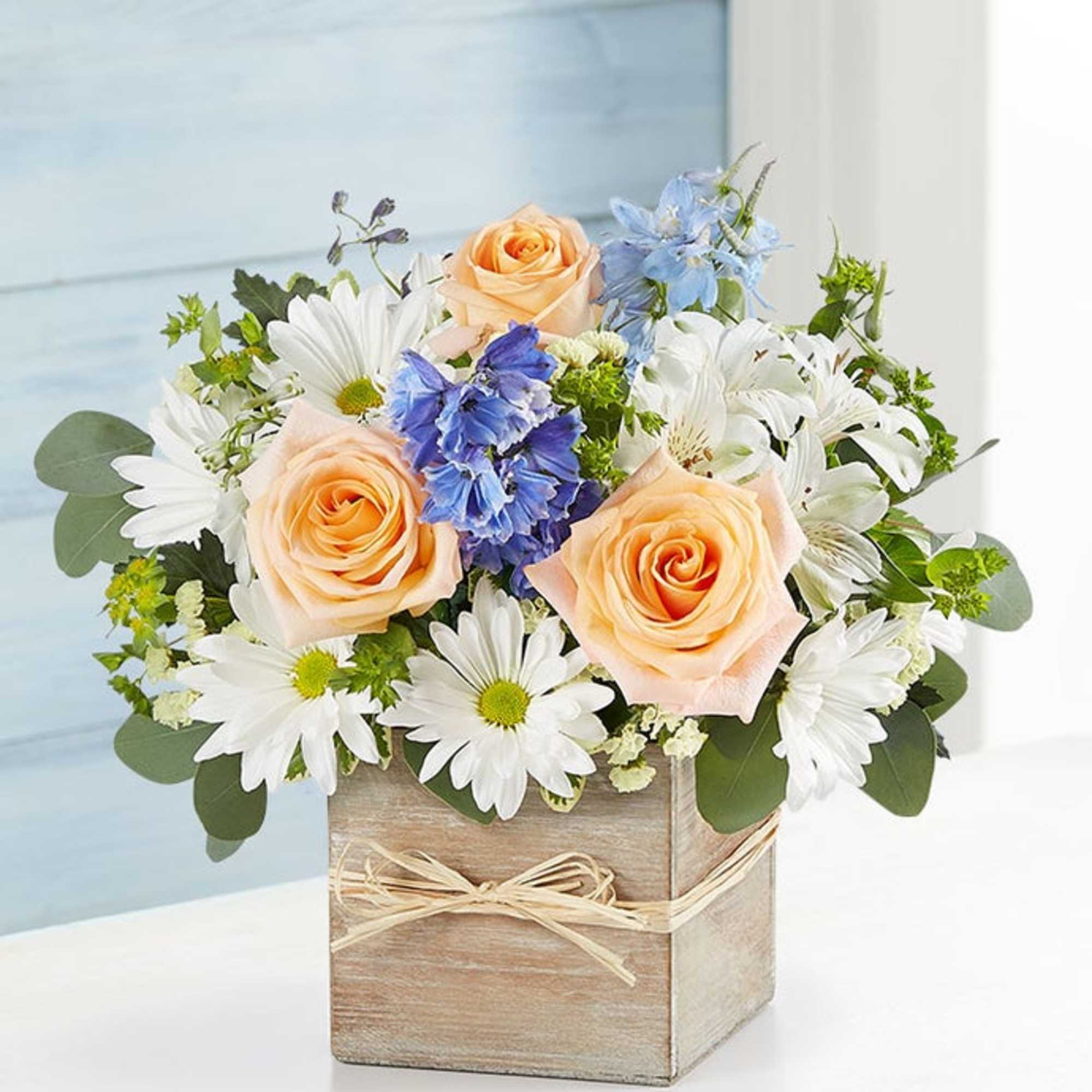 Bouquet of peach roses, white daisies, and blue flowers in a wooden box