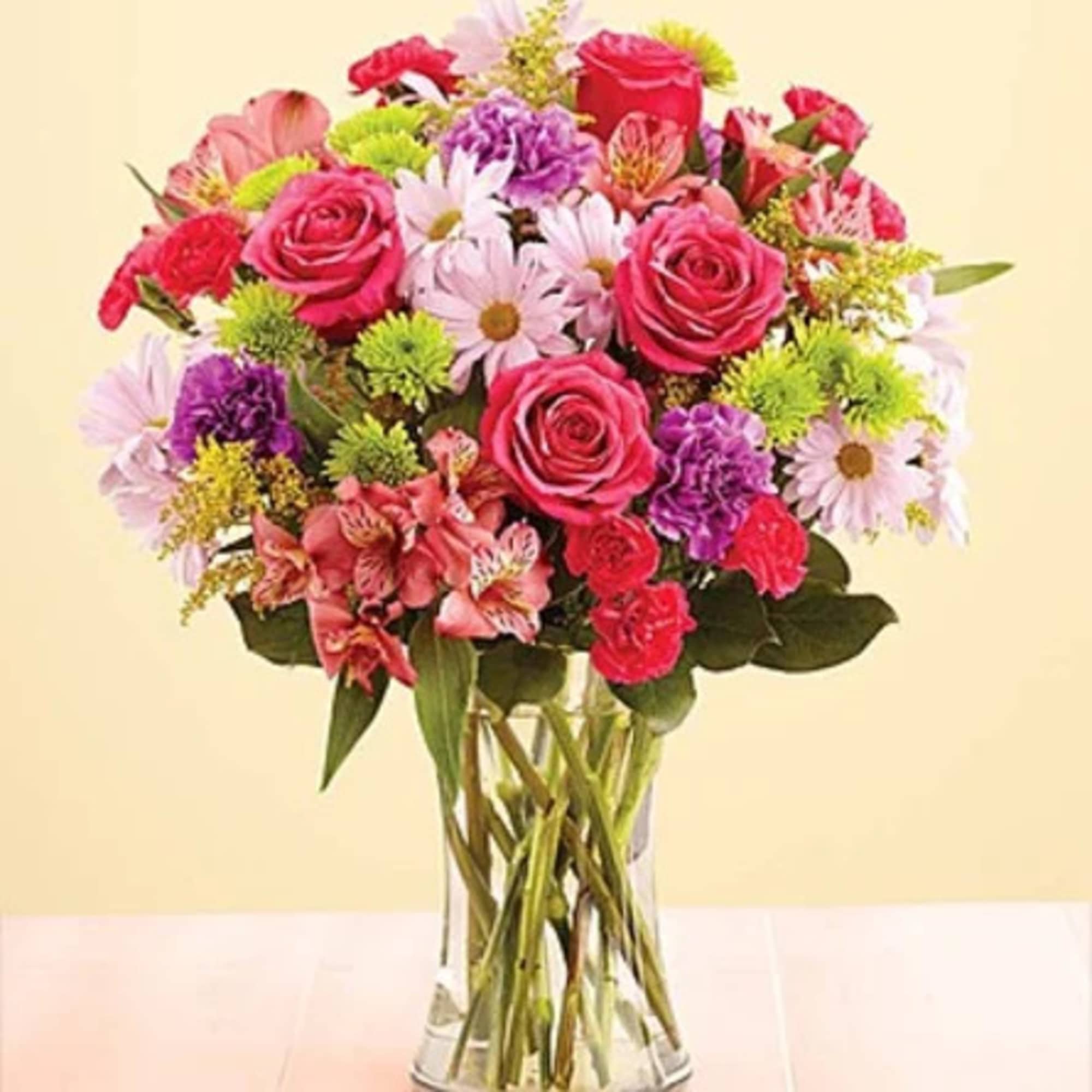 Mixed bouquet of pink roses, daisies, and carnations in a clear glass vase