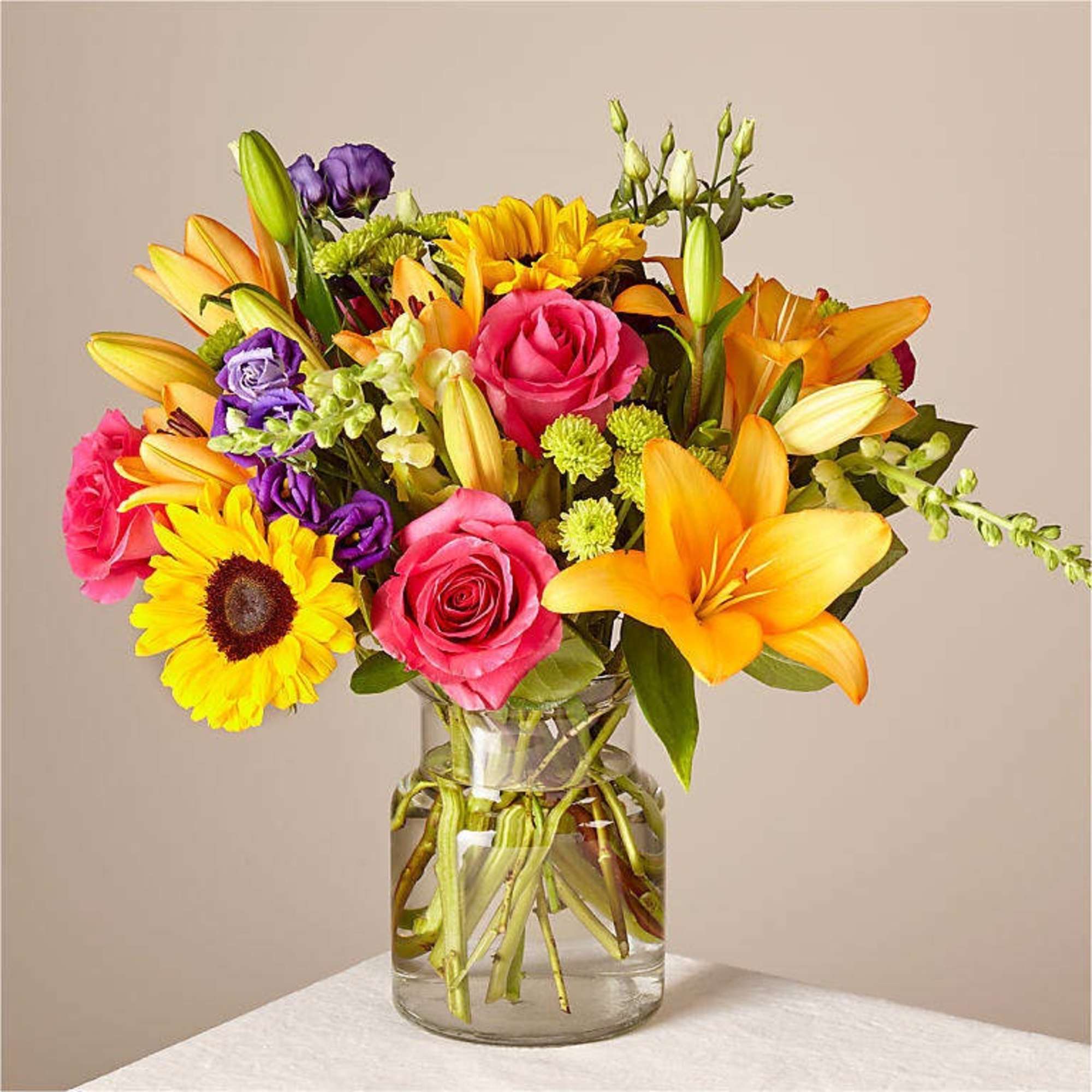 Mixed bouquet of lilies, roses, and a sunflower in a glass vase