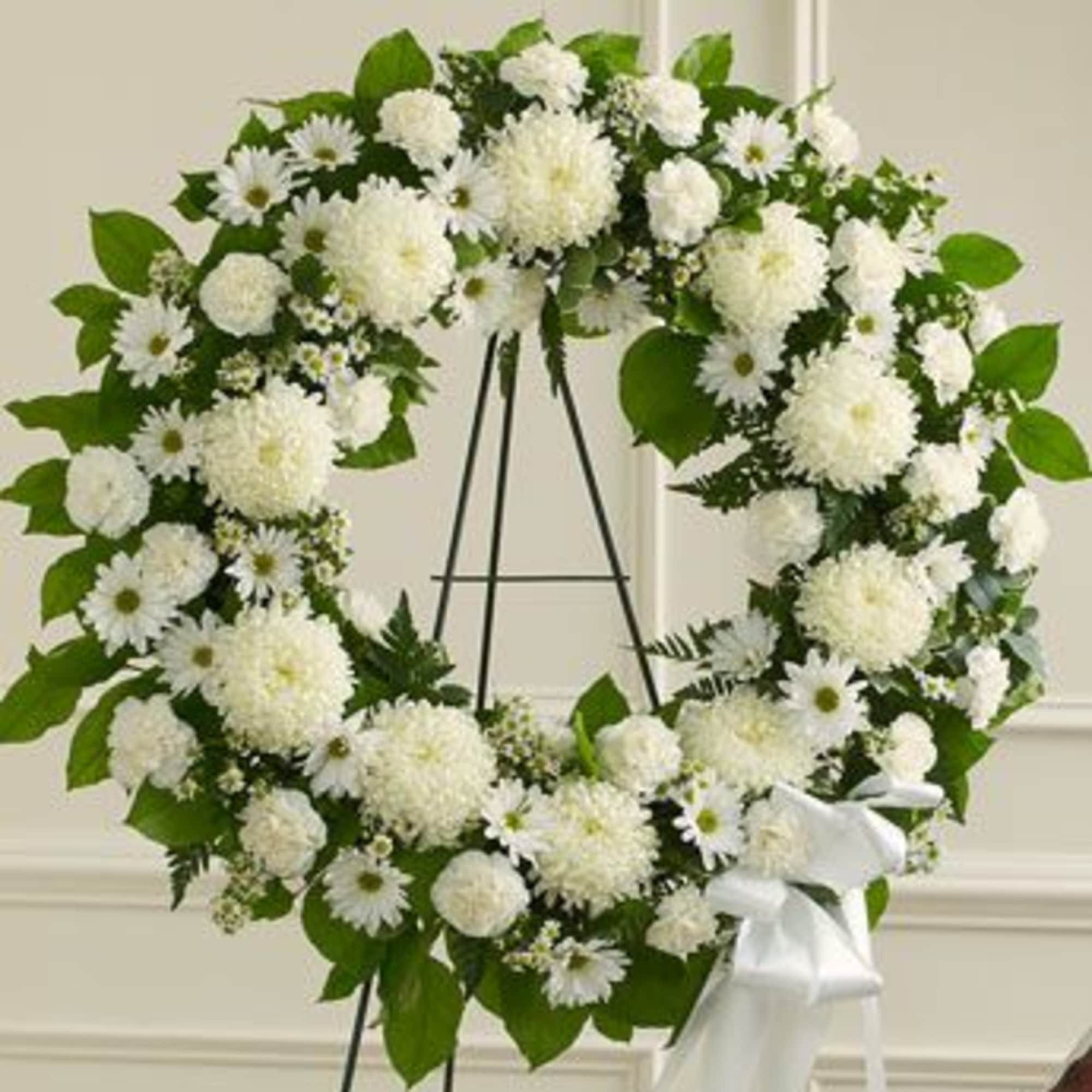White floral wreath on a black easel with a white ribbon