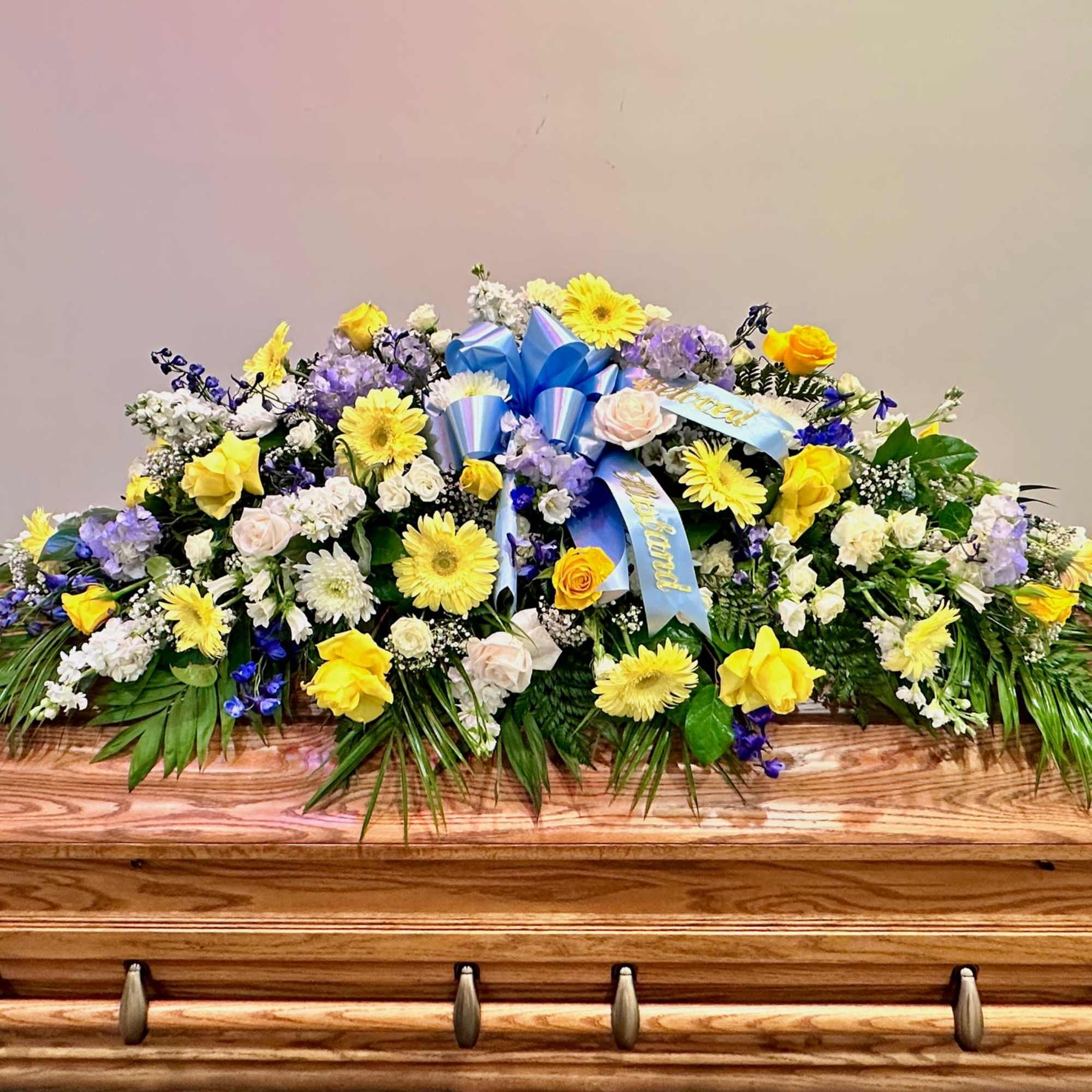 Large floral casket spray with yellow, white, and purple flowers