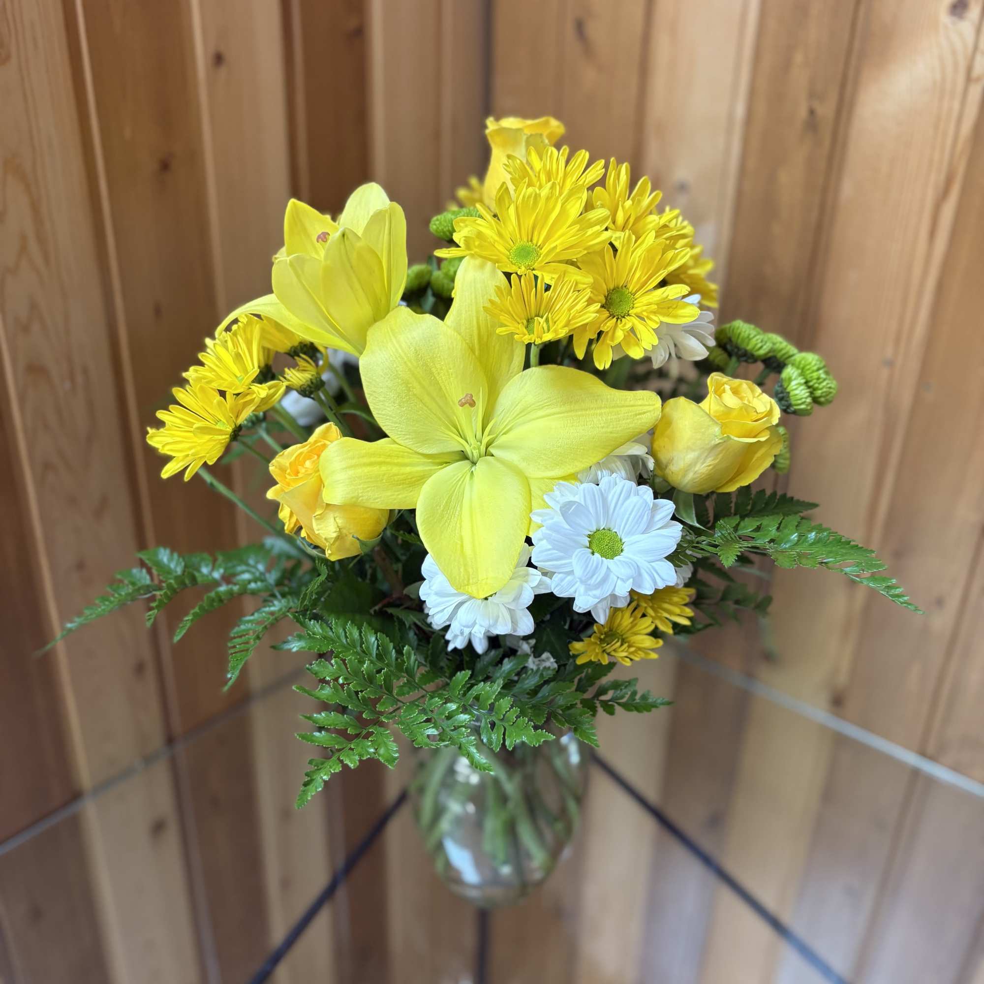 Yellow lilies and daisies in a clear glass vase