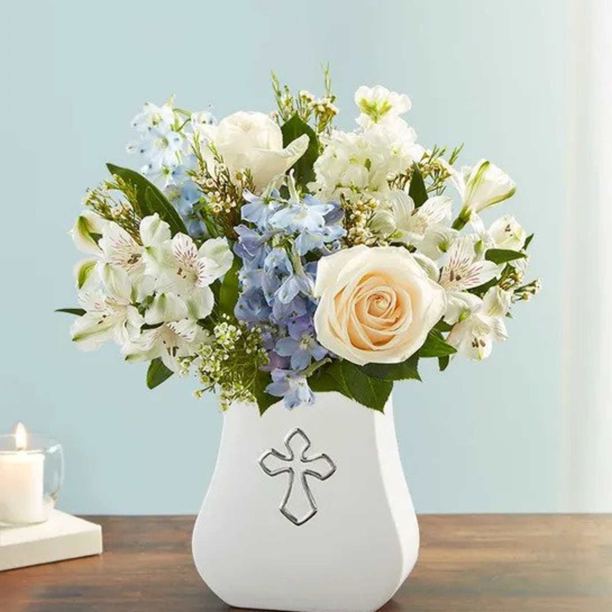 White and cream roses with blue and white blooms in a white vase with a cross emblem