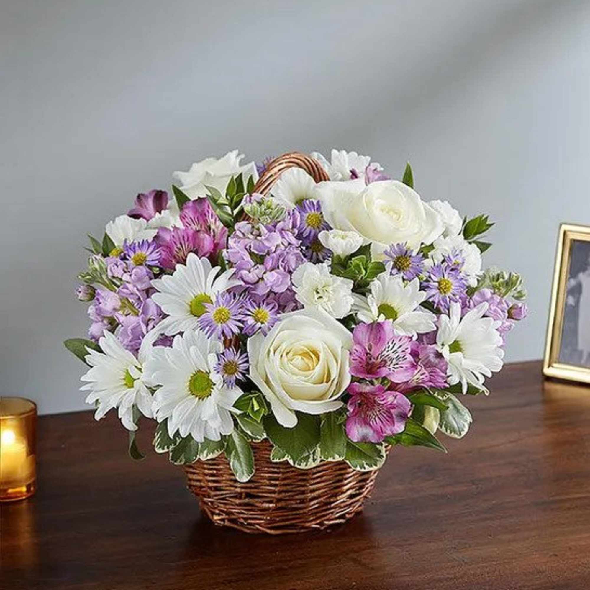 Basket arrangement of white roses, daisies, and purple flowers on a wooden table