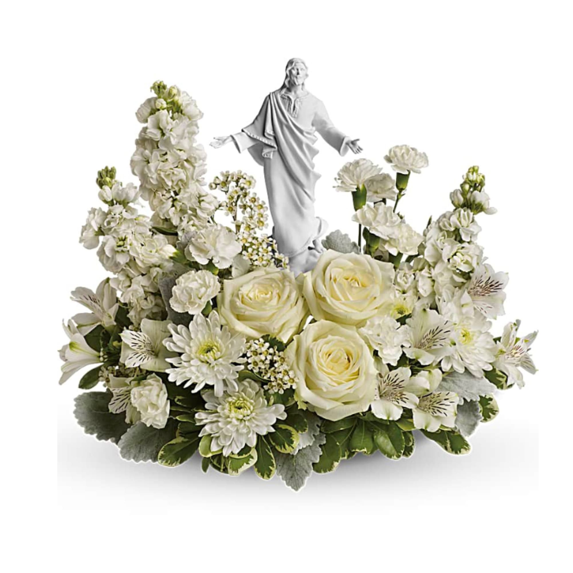 Low white floral arrangement with roses and other blooms surrounding a white Jesus figurine.