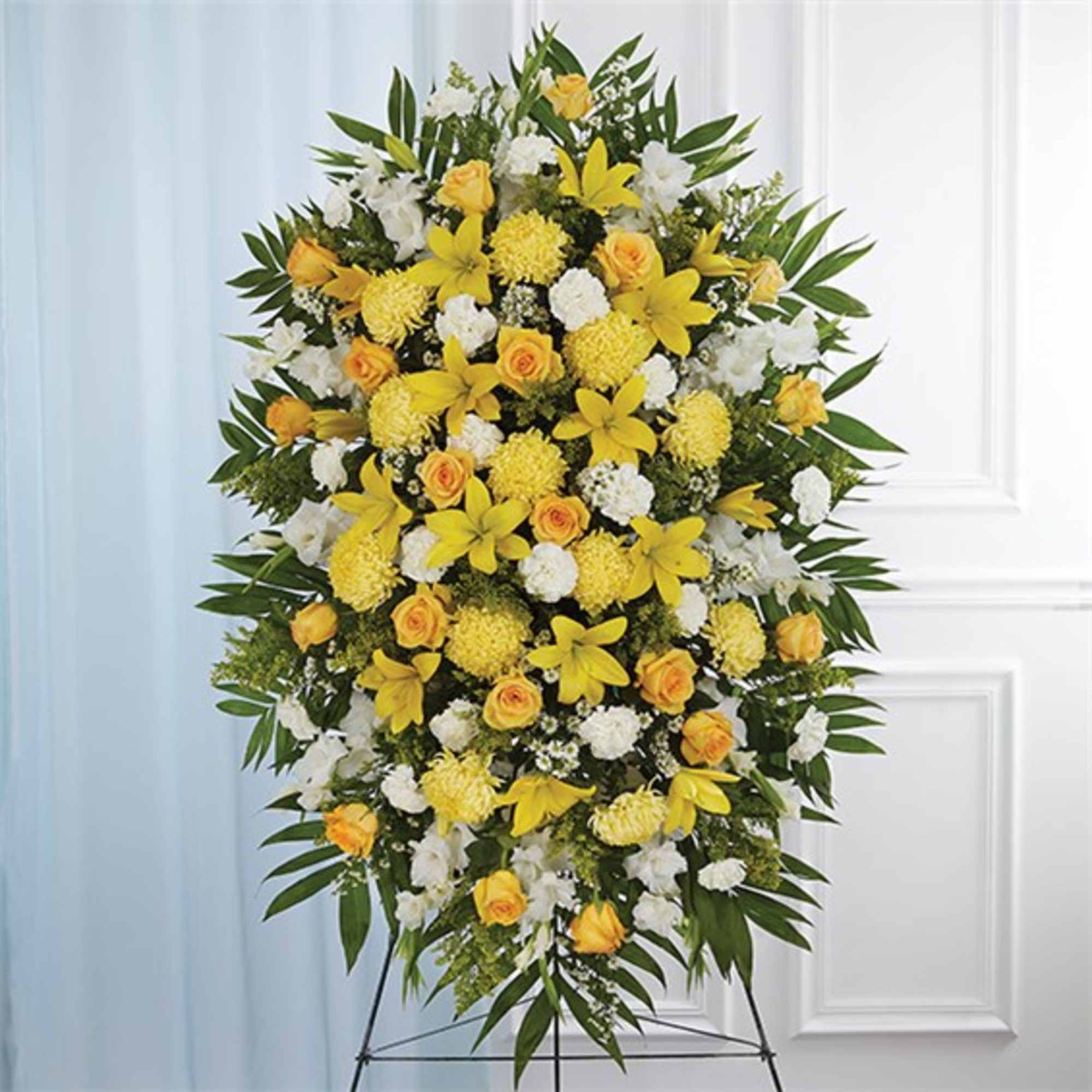 Standing spray of yellow lilies and roses with white flowers on a metal easel