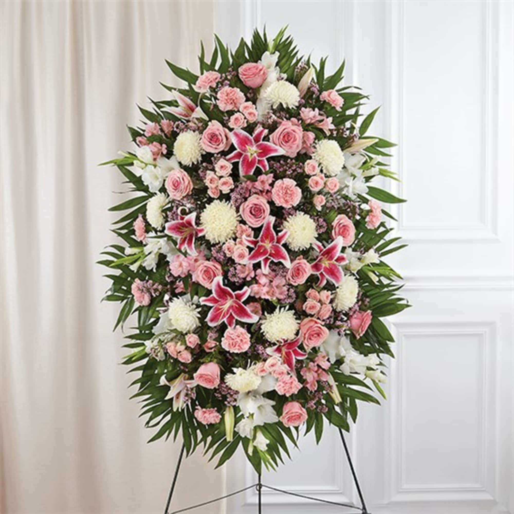Tall oval standing spray of pink roses, lilies, and white mums on an easel.