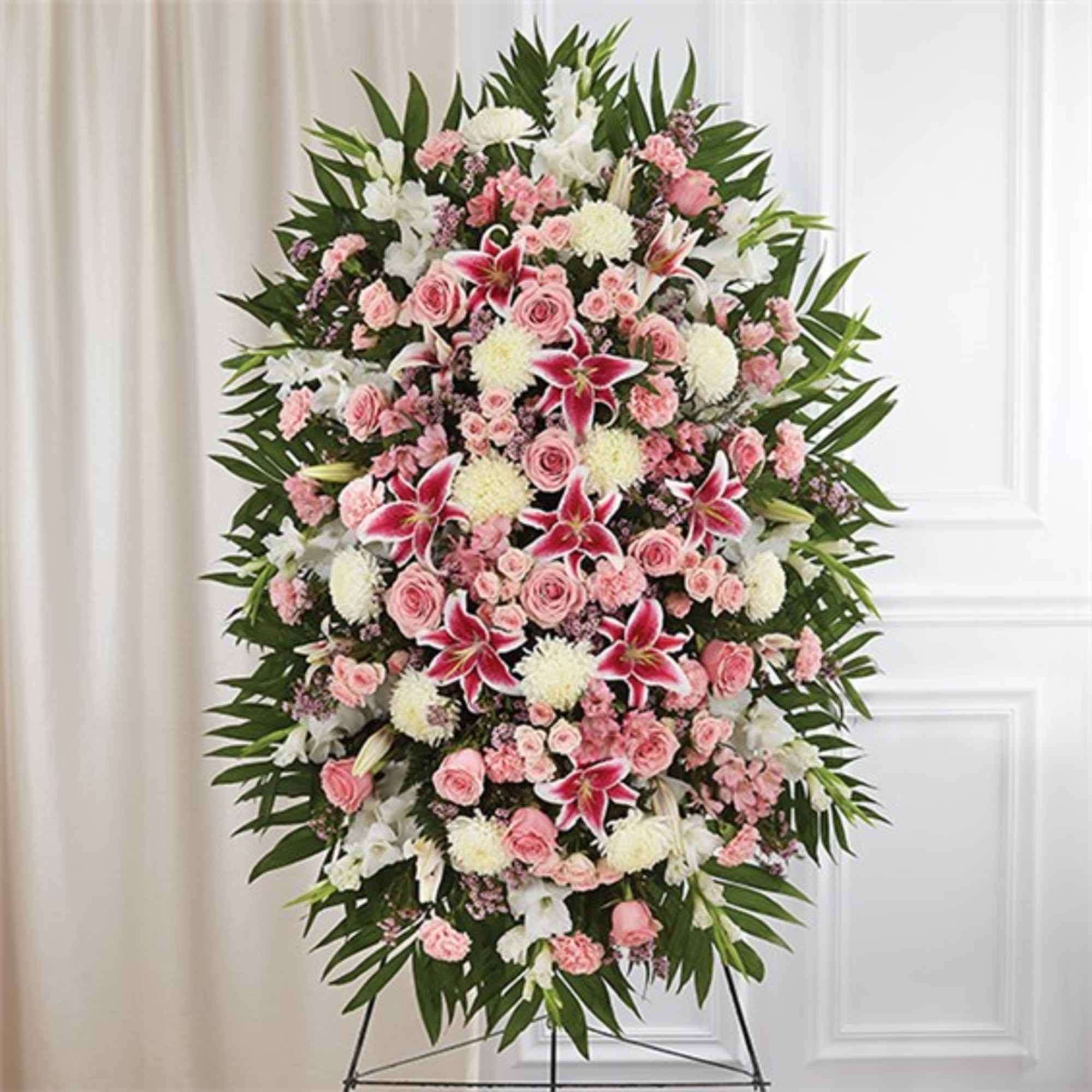 Tall standing spray of pink roses, carnations, and lilies with white mums on an easel
