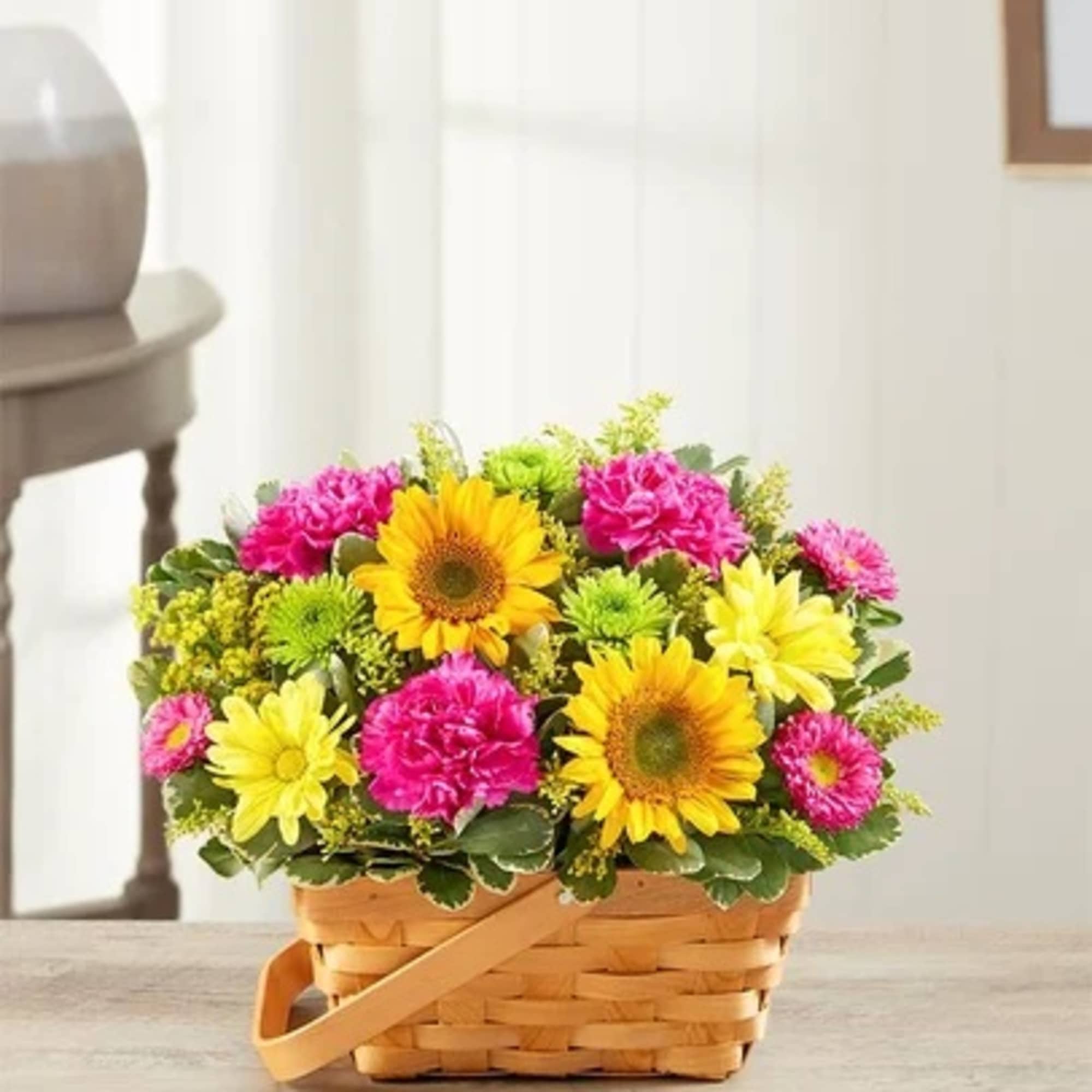 Bright basket arrangement of yellow sunflowers, pink carnations, and yellow and green mums.