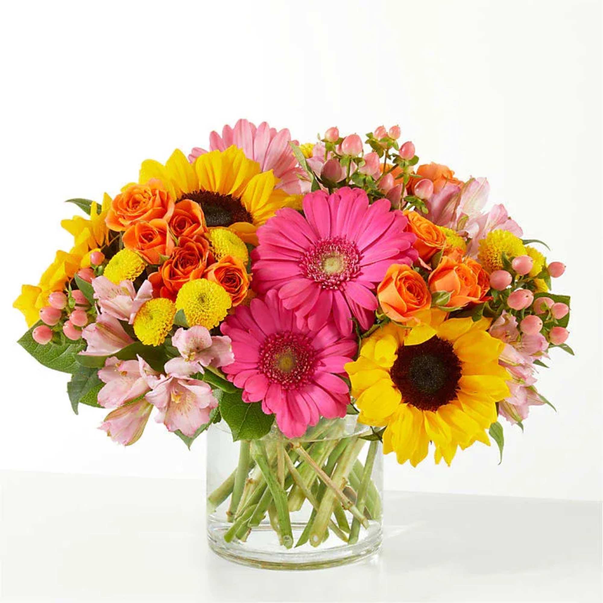 Bright arrangement of sunflowers, pink gerbera daisies and orange roses in a clear glass vase