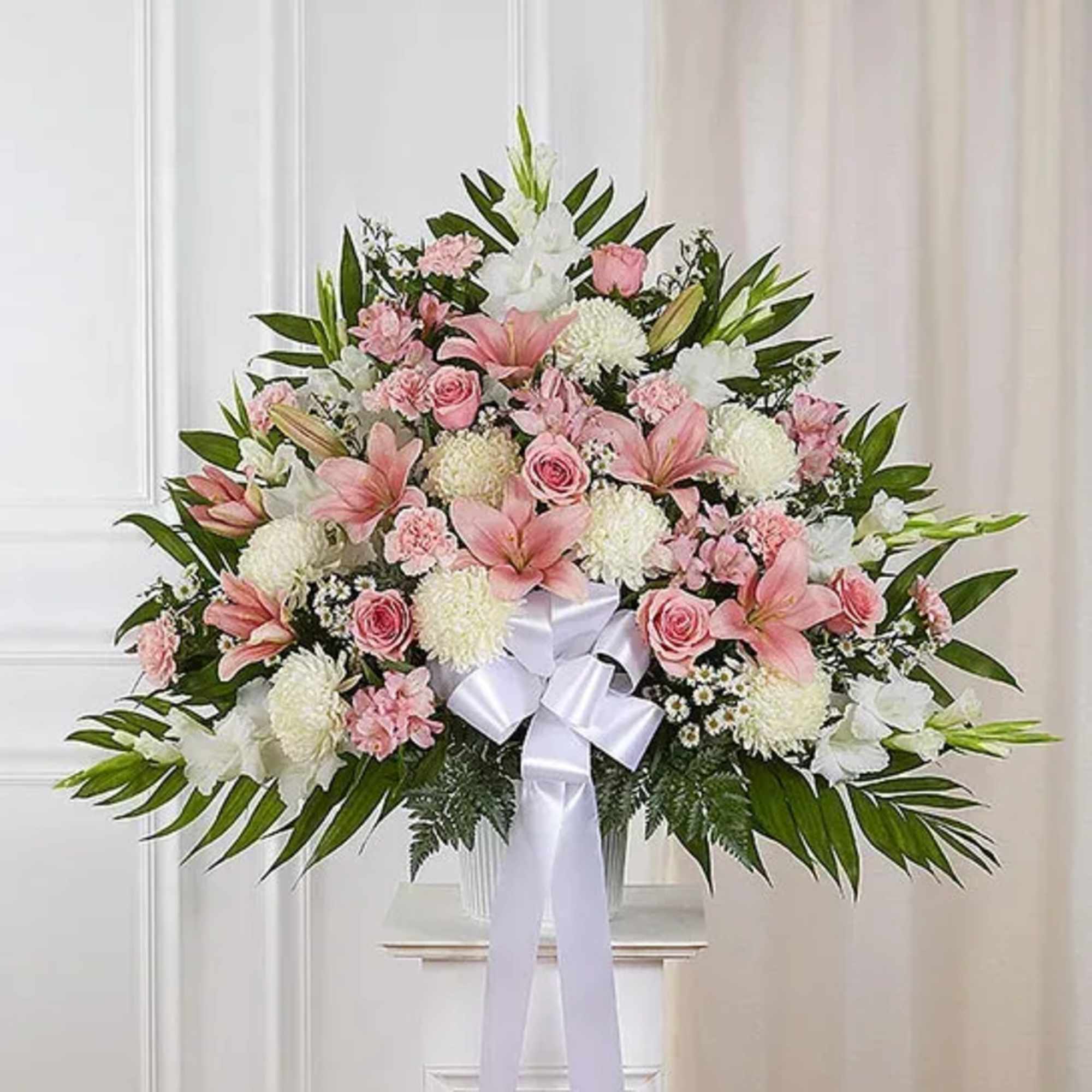 Large pink and white floral arrangement with a white bow displayed on a pedestal