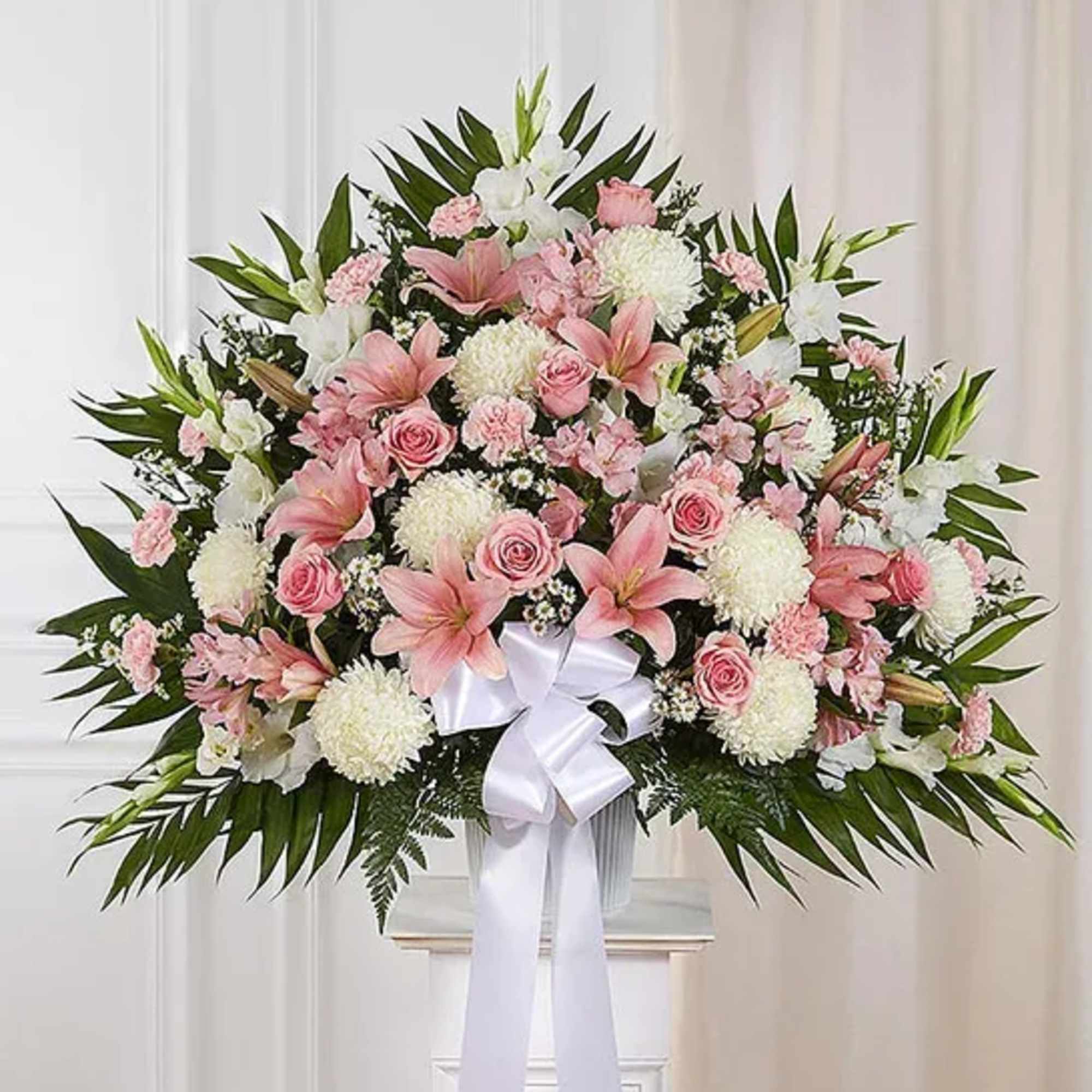 Large fan-shaped pink and white flower arrangement with a white ribbon bow on a pedestal.