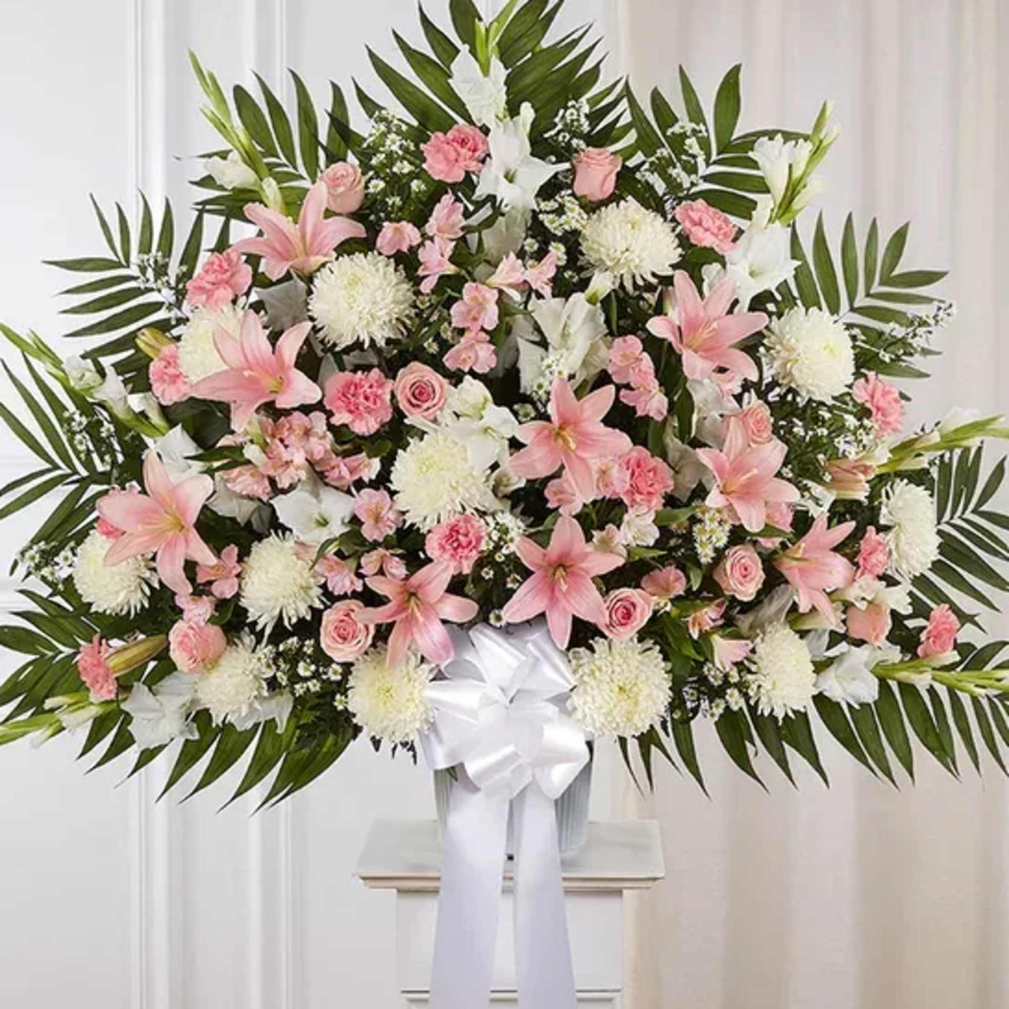 Large standing arrangement of pink lilies and roses with white flowers and bow on a pedestal