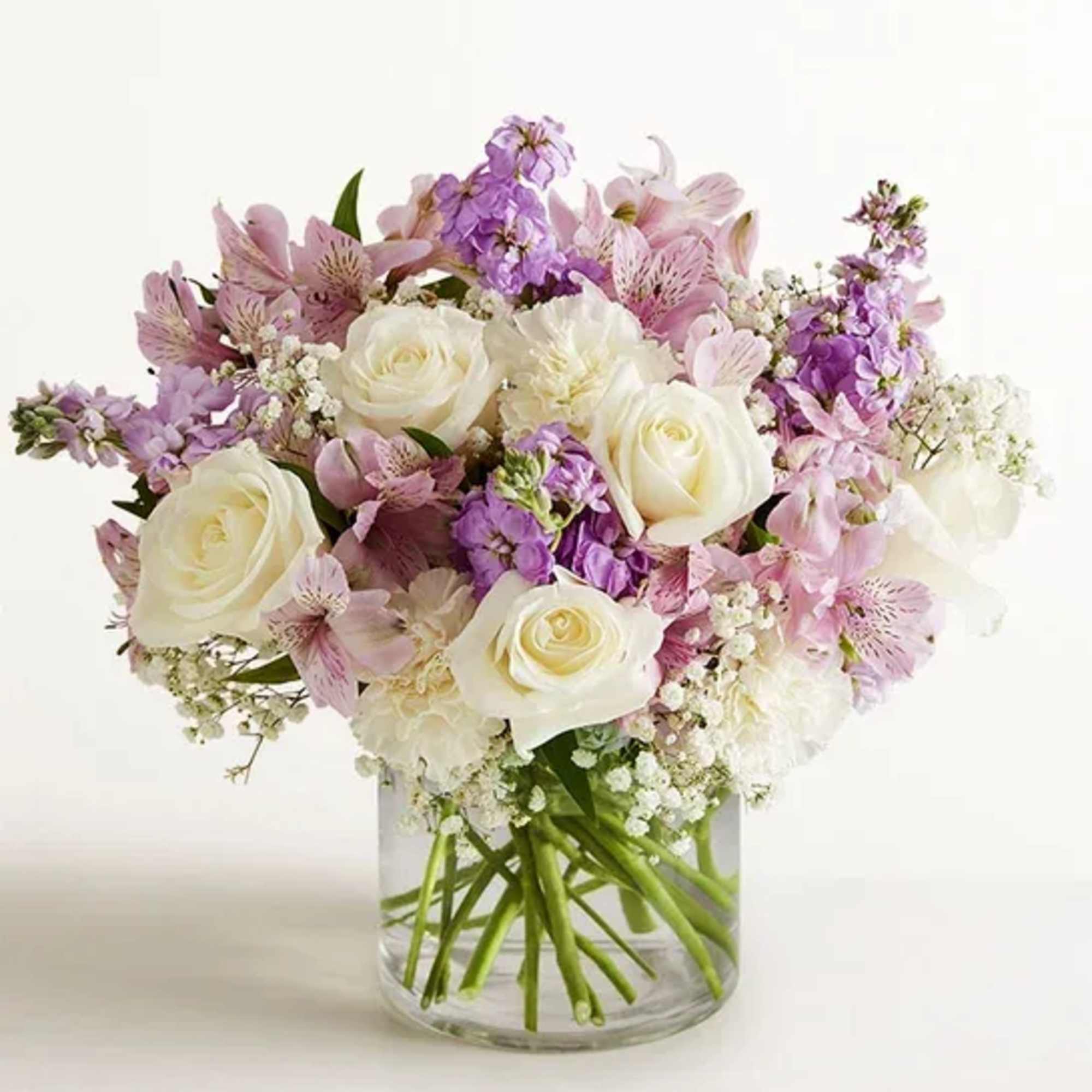 Pastel bouquet of white roses and purple flowers in a clear glass cylinder vase