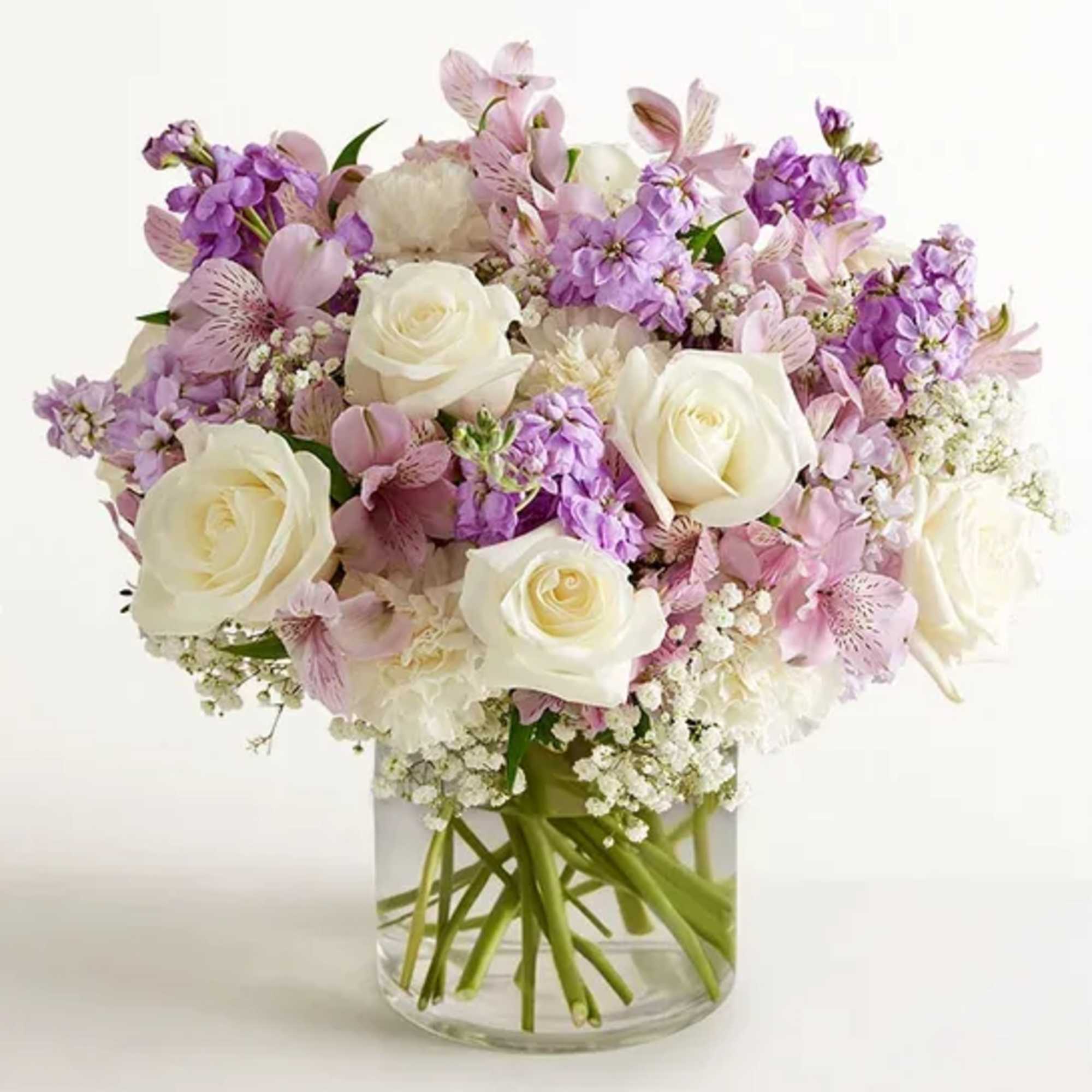 Round arrangement of white roses, lavender stock, and pink alstroemeria in a clear glass vase
