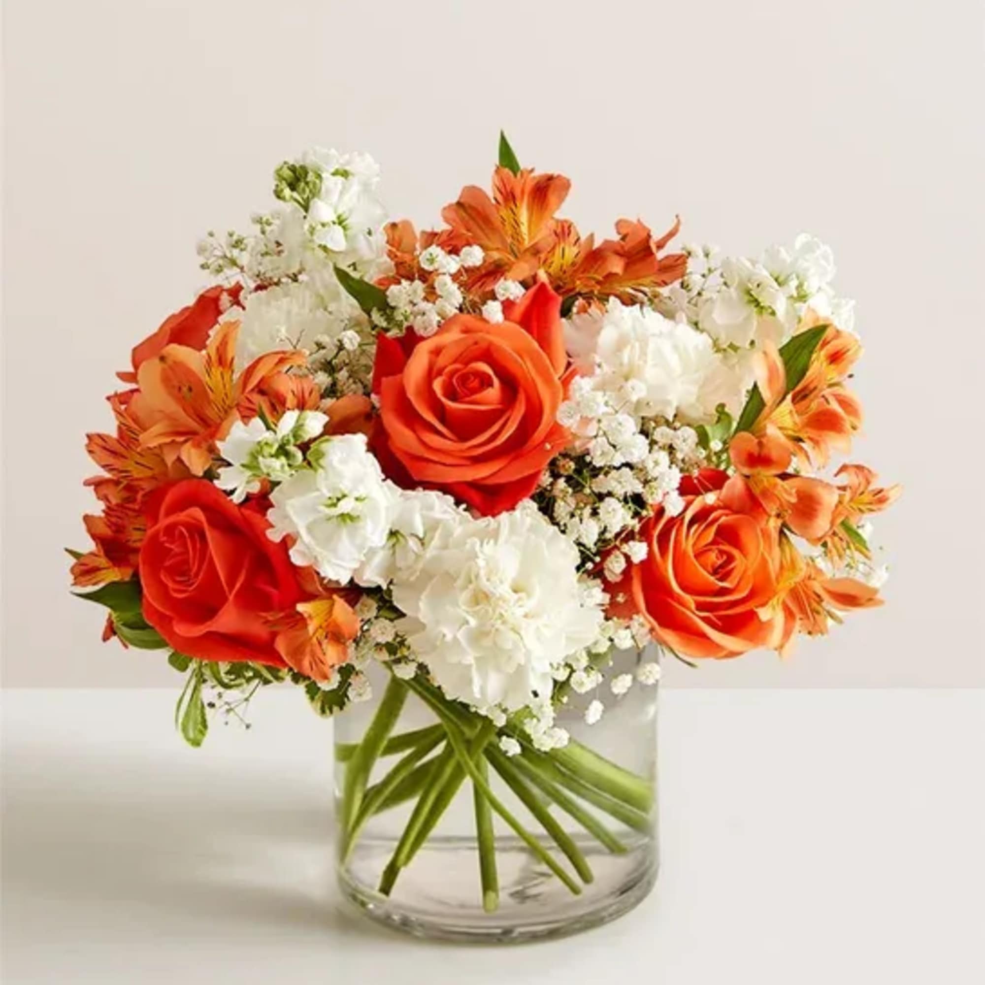 Compact bouquet of orange roses and white flowers in a clear glass vase