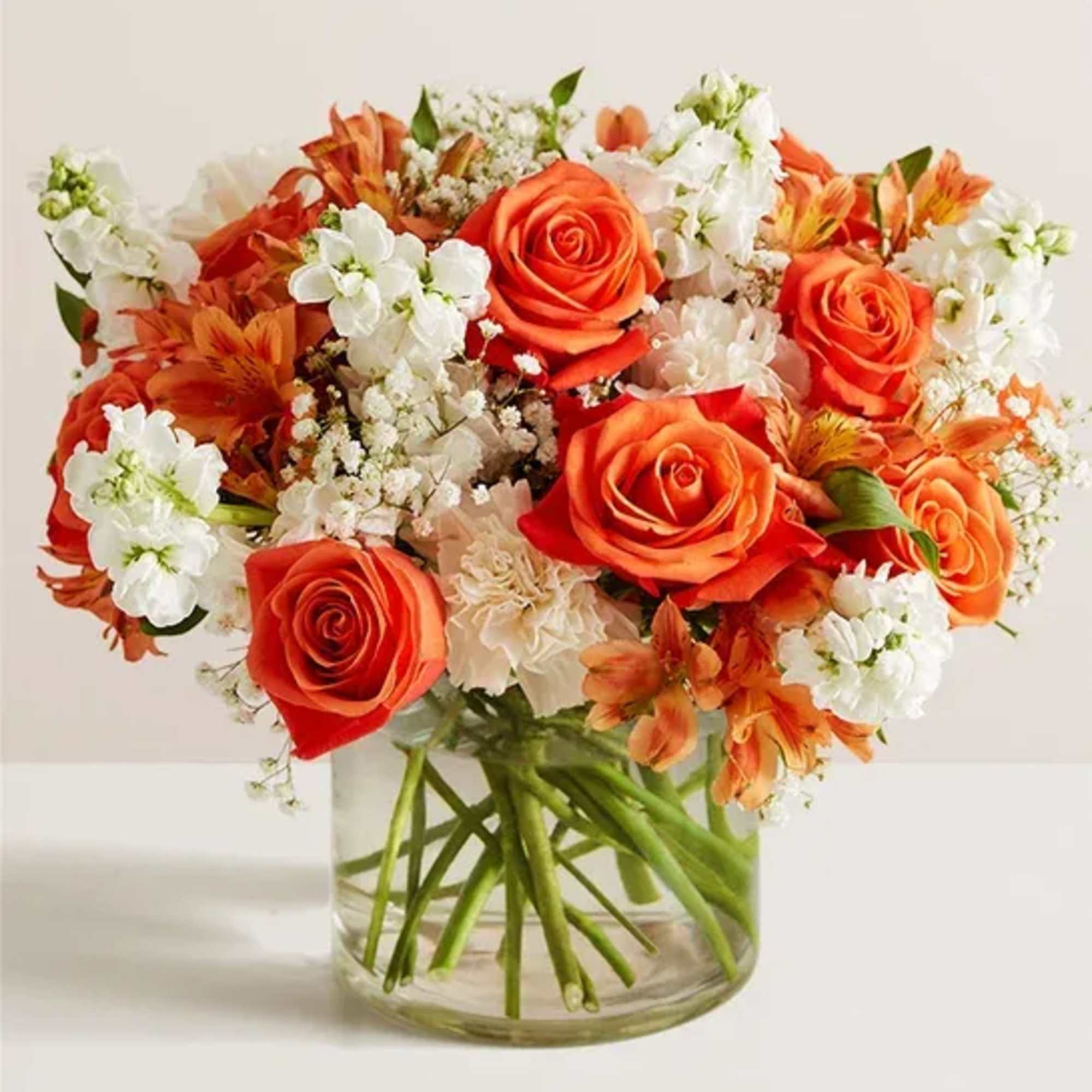 Compact bouquet of orange roses and white flowers in a clear glass cylinder vase