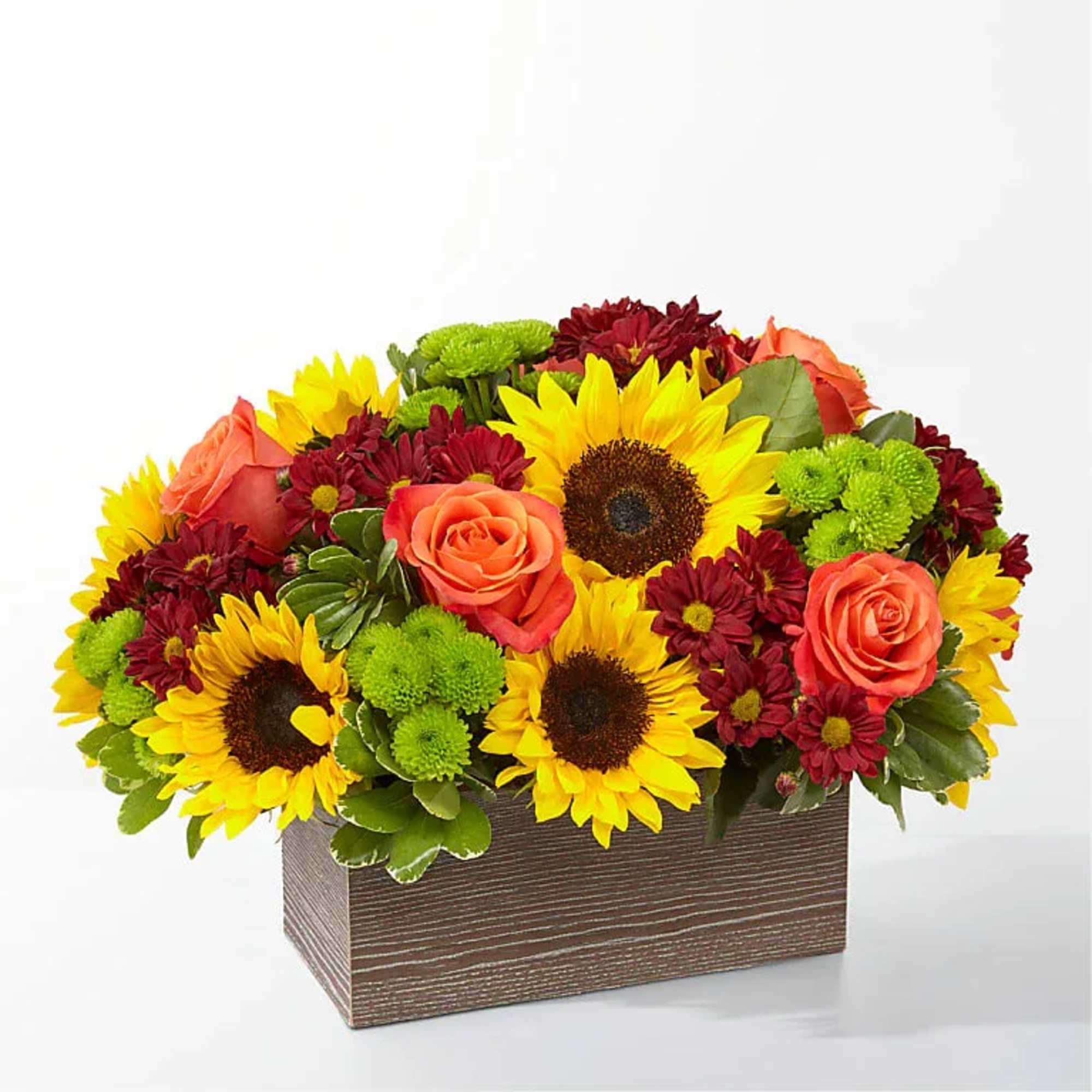 Low box arrangement of yellow sunflowers, orange roses, and red blossoms in a rectangular container.