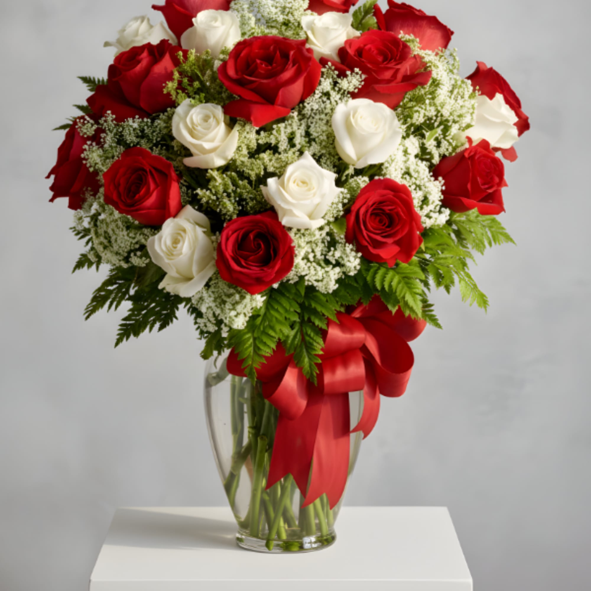 Red and white roses in a clear glass vase with a red ribbon
