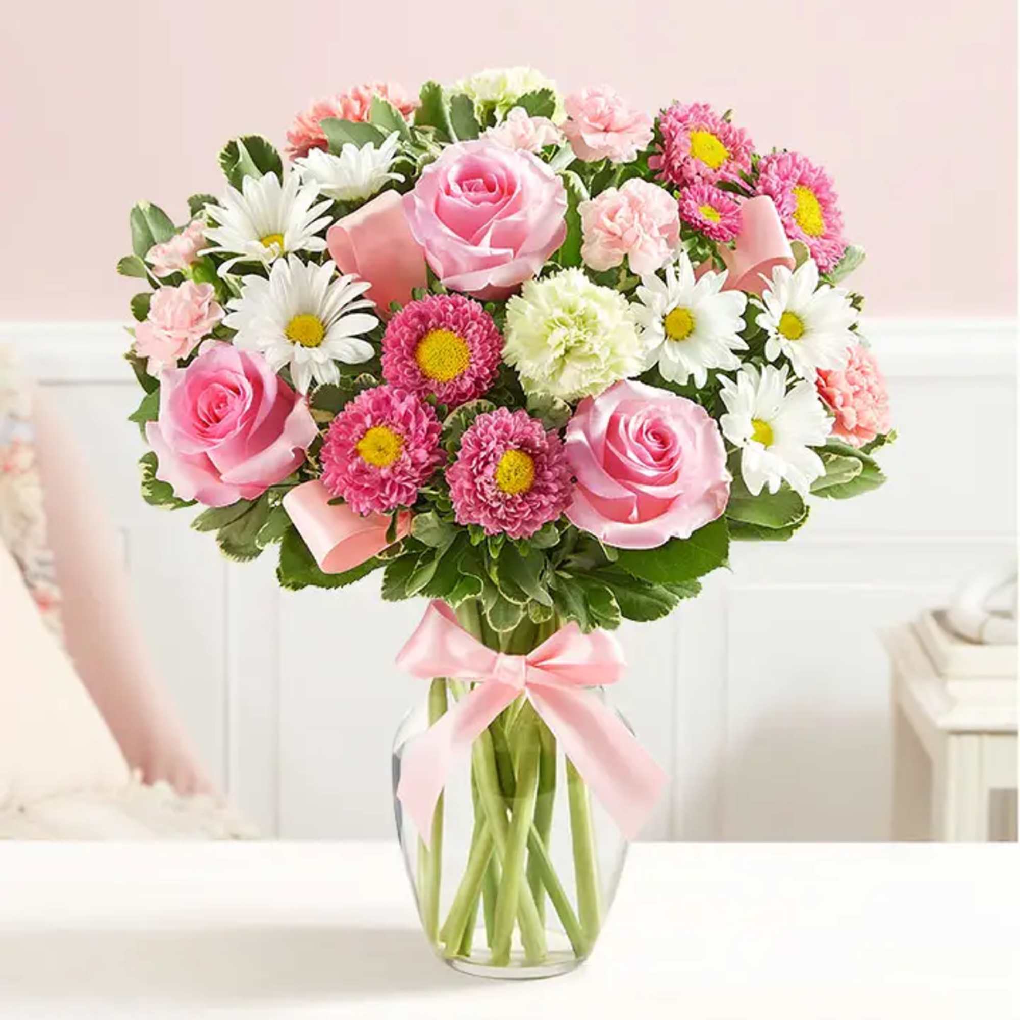 Pink roses and daisies arranged in a clear glass vase with a pink ribbon