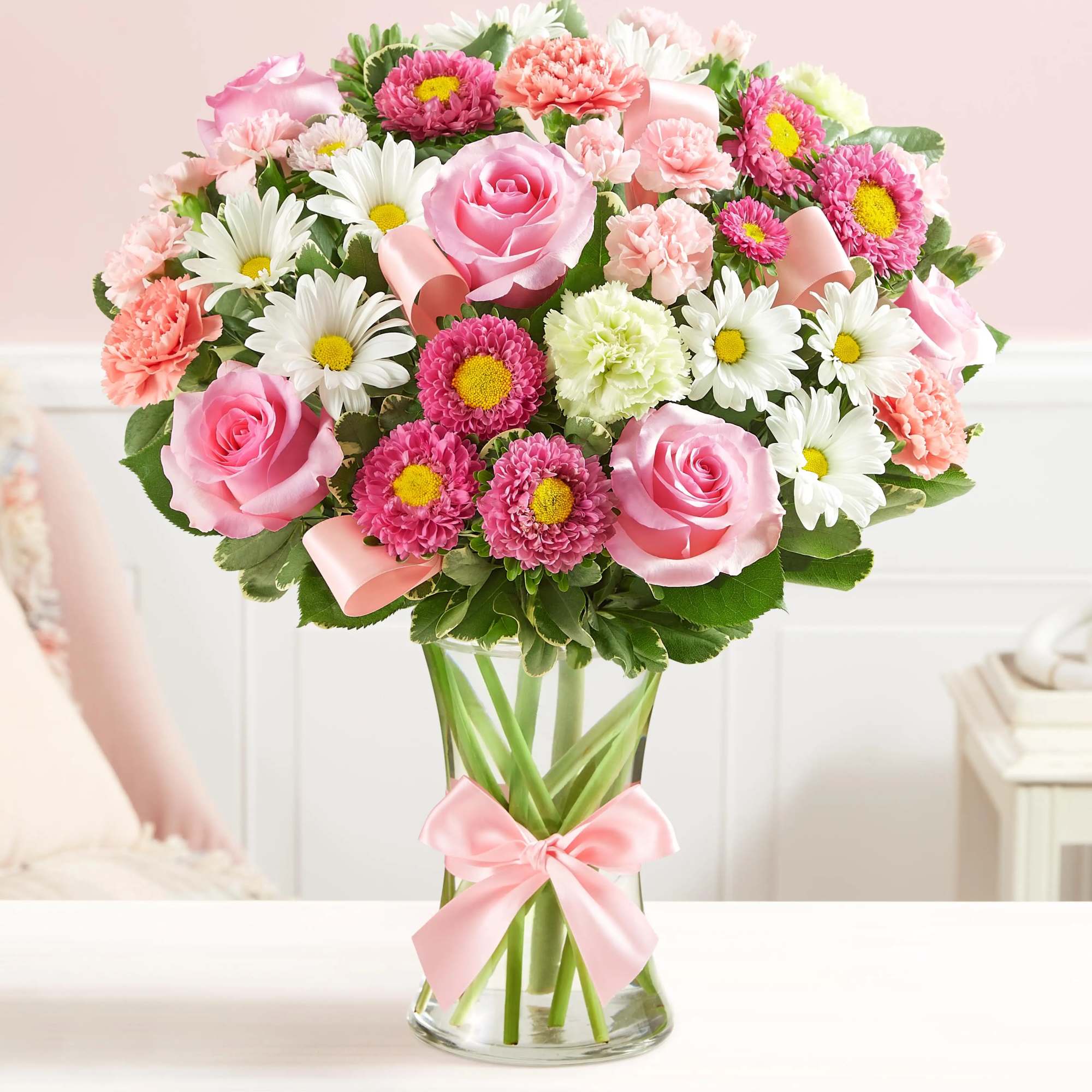 Pink roses and daisies arranged in a clear glass vase with a pink ribbon